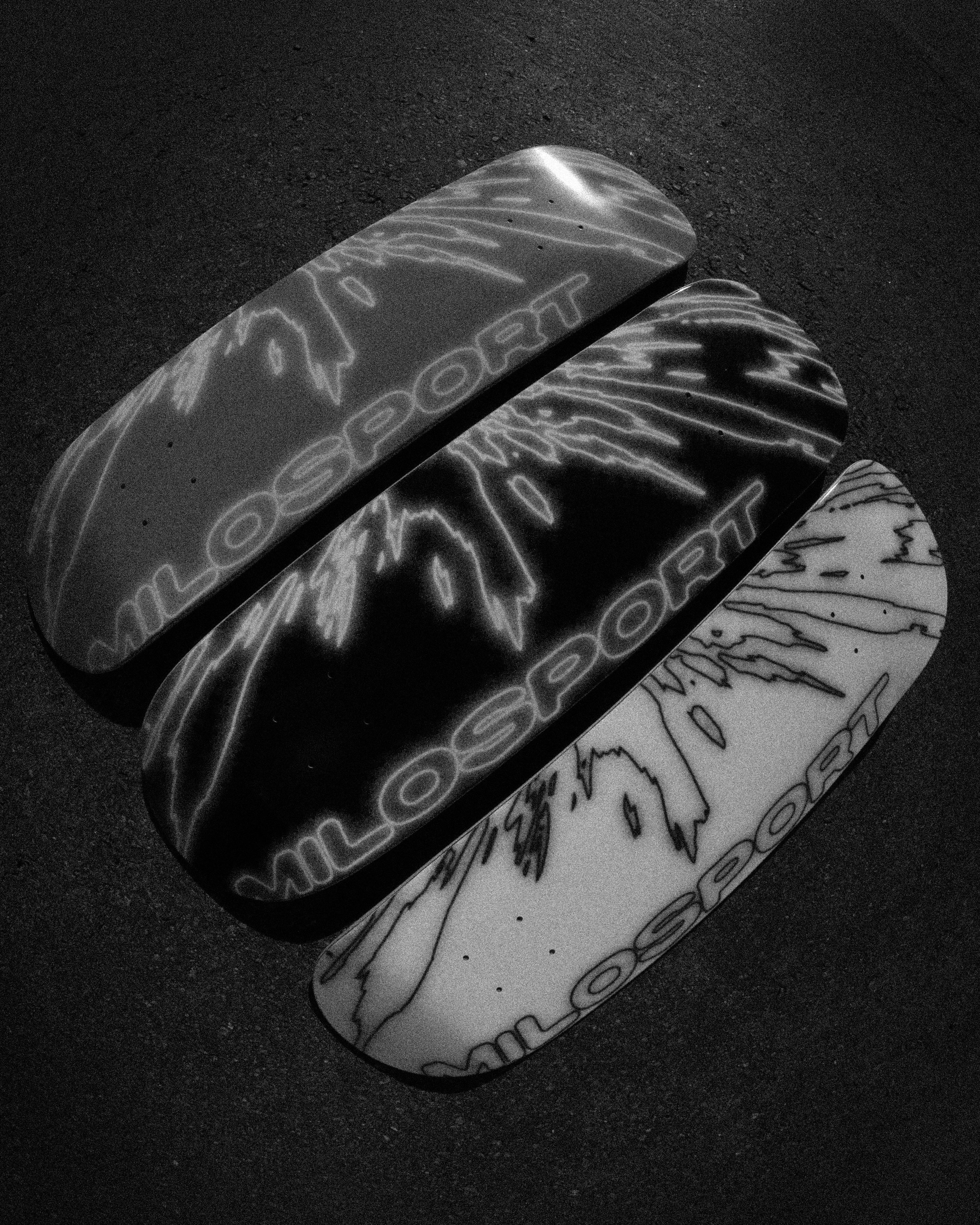 Black and white image of three Milosport Elbow Fracture skateboard decks displayed together on pavement, used for the Milosport Decks collection.