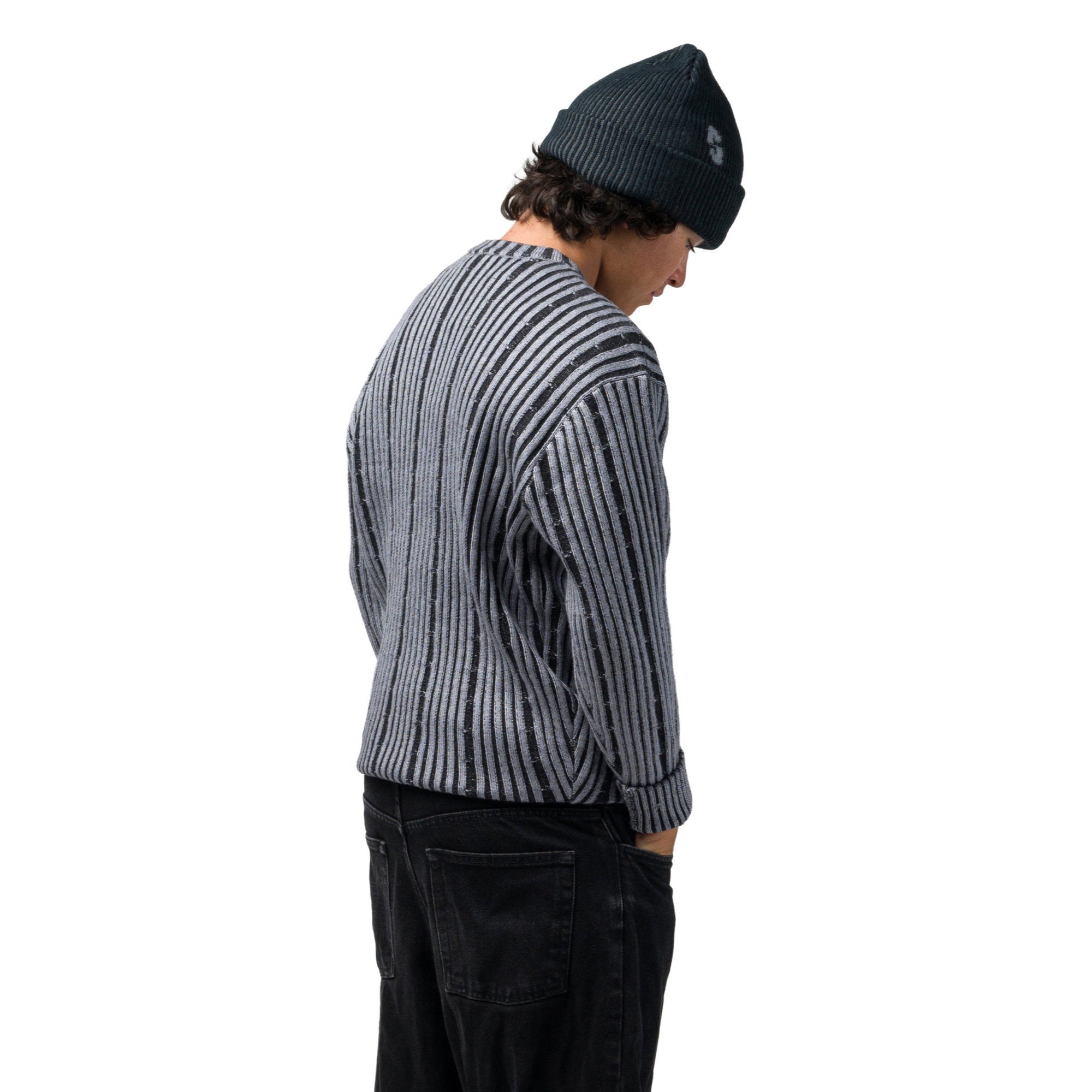 A person shown from the back wearing a dark ribbed knit beanie, a gray and black vertically striped knit souvenir chunky sweater, and black jeans, against a plain white background.