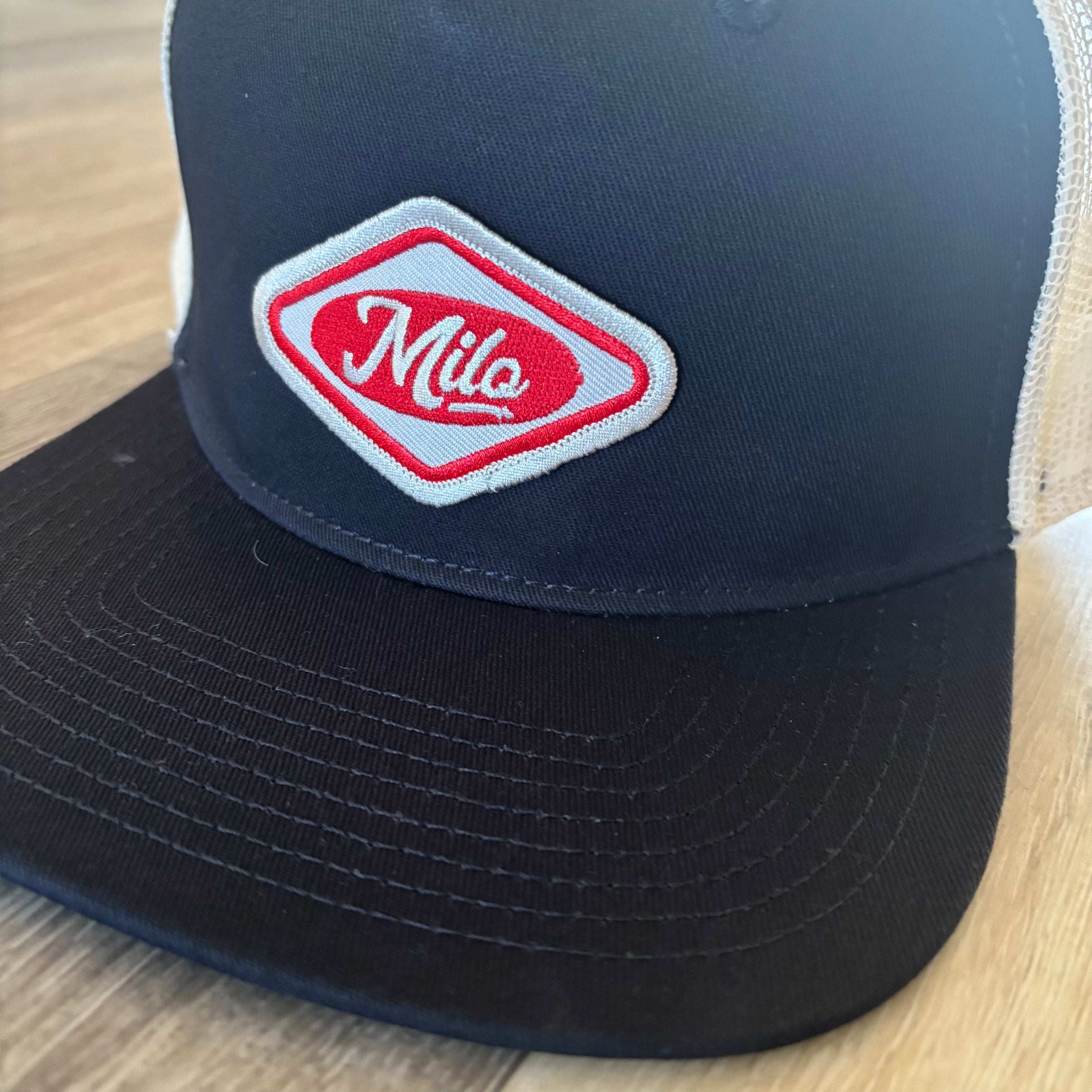 Milosport House Deli contrast trucker hat for men with embroidered logo and mesh back, adjustable snap closure.