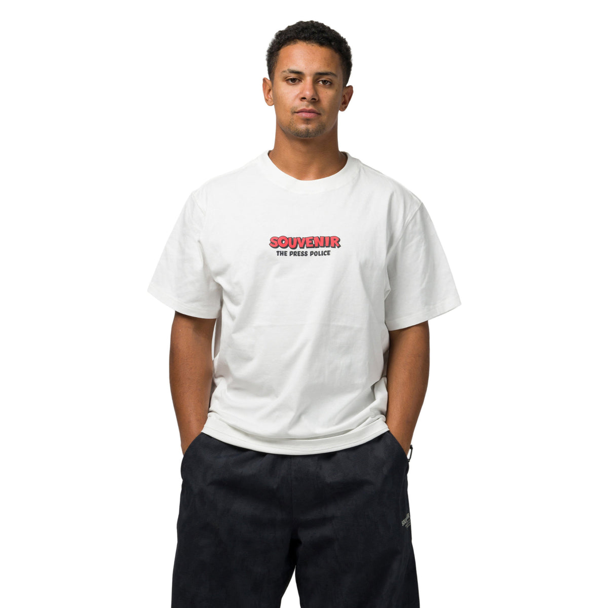 A man wearing a white crewneck t-shirt with a red and black 'SOUVENIR THE FEELING' graphic on the chest, paired with dark pants, against a plain white background.