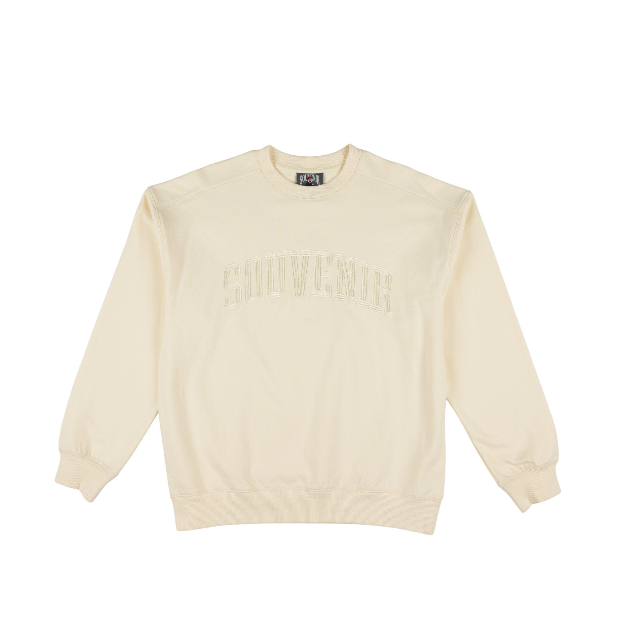 An off-white crewneck sweatshirt with 'SOUVENIRS printed in a tonal, arched font across the chest, displayed flat against a solid white background.