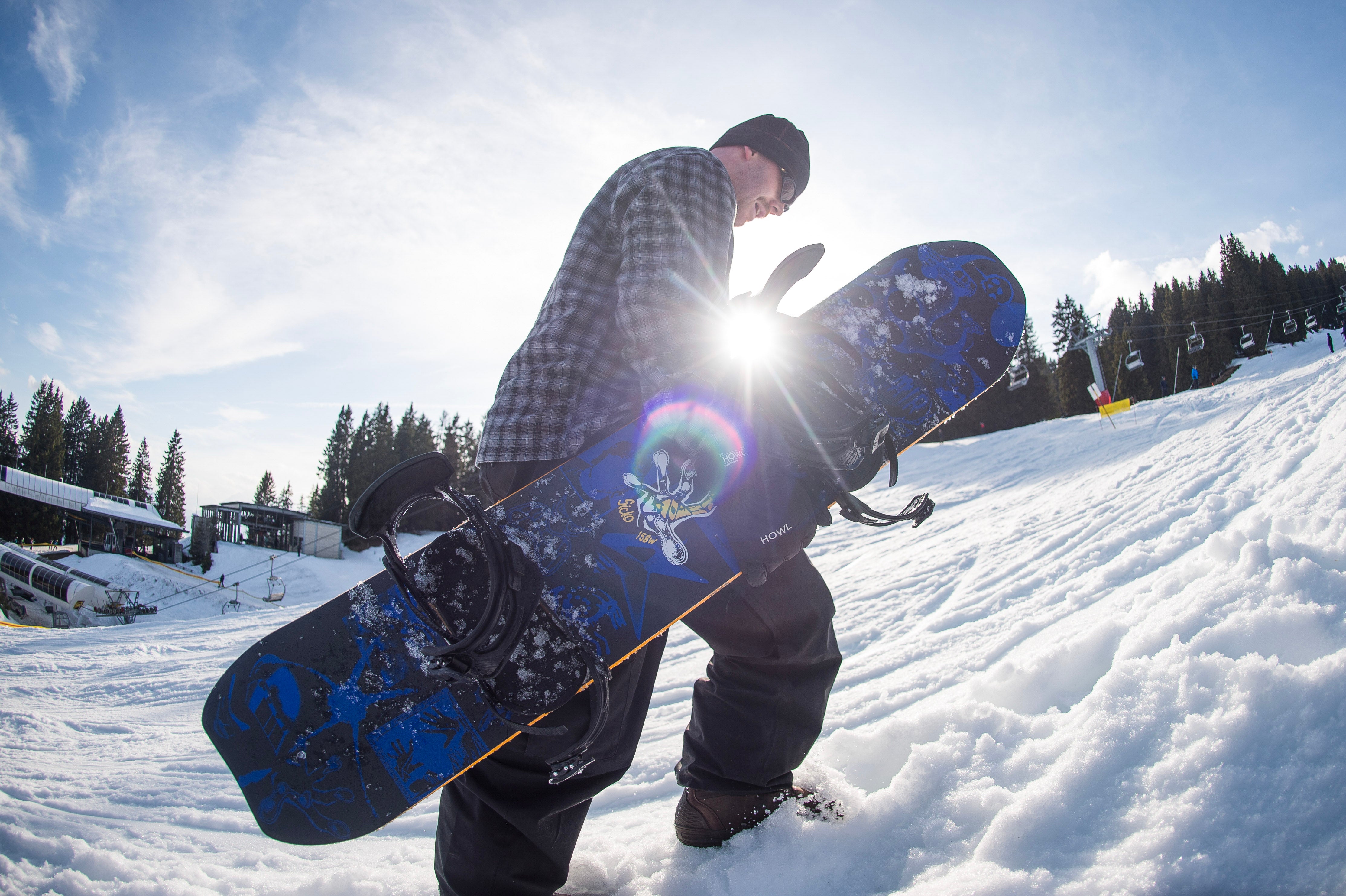 Armada Sicko snowboard in winter snow, featuring a rider hiking in snowy mountain terrain, showcasing the snowboard's design and durability.