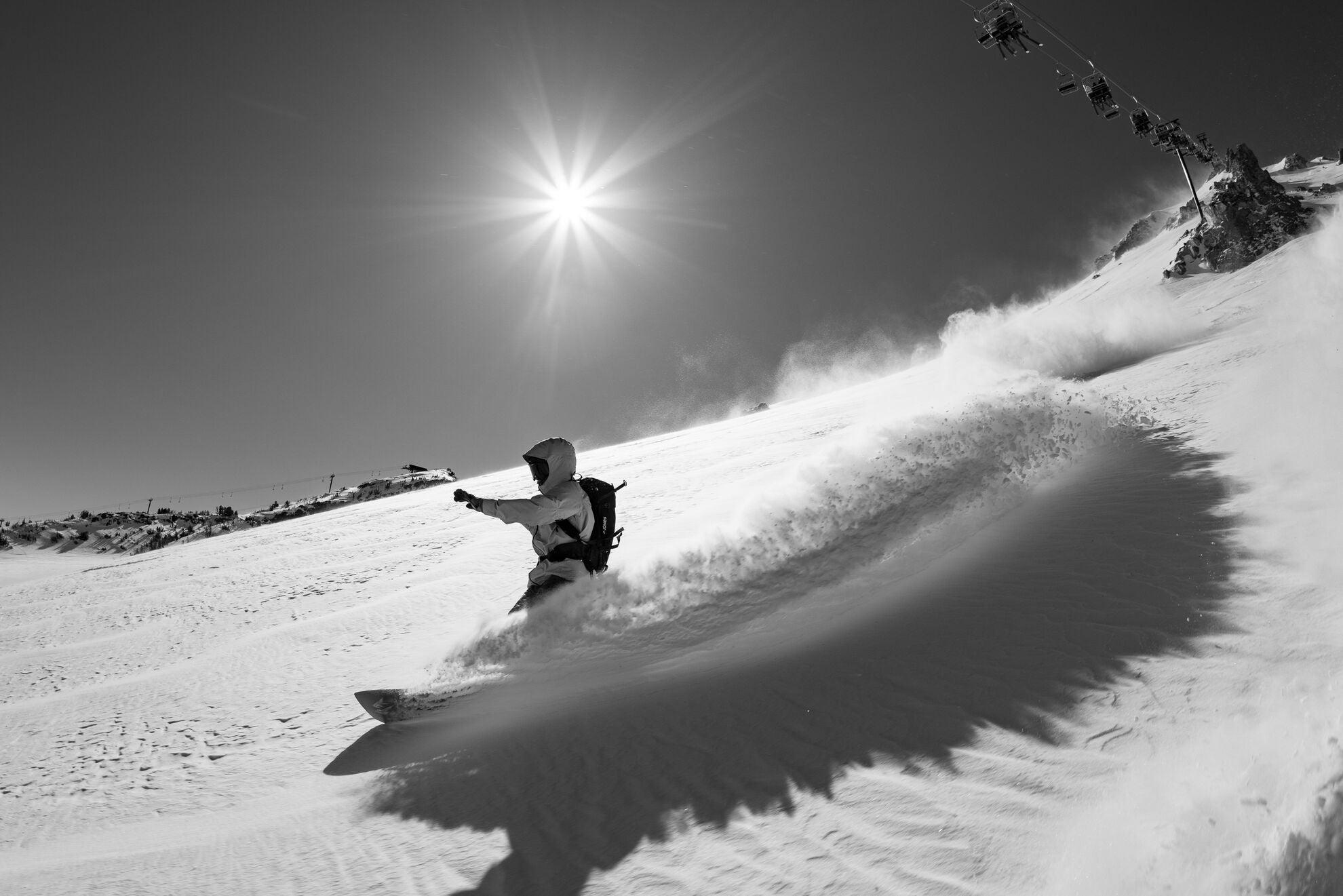 Jones Men's Frontier 2 Snowboard for 2027, shown in powder snow with sunlight, highlighting its durable design and sleek graphics.