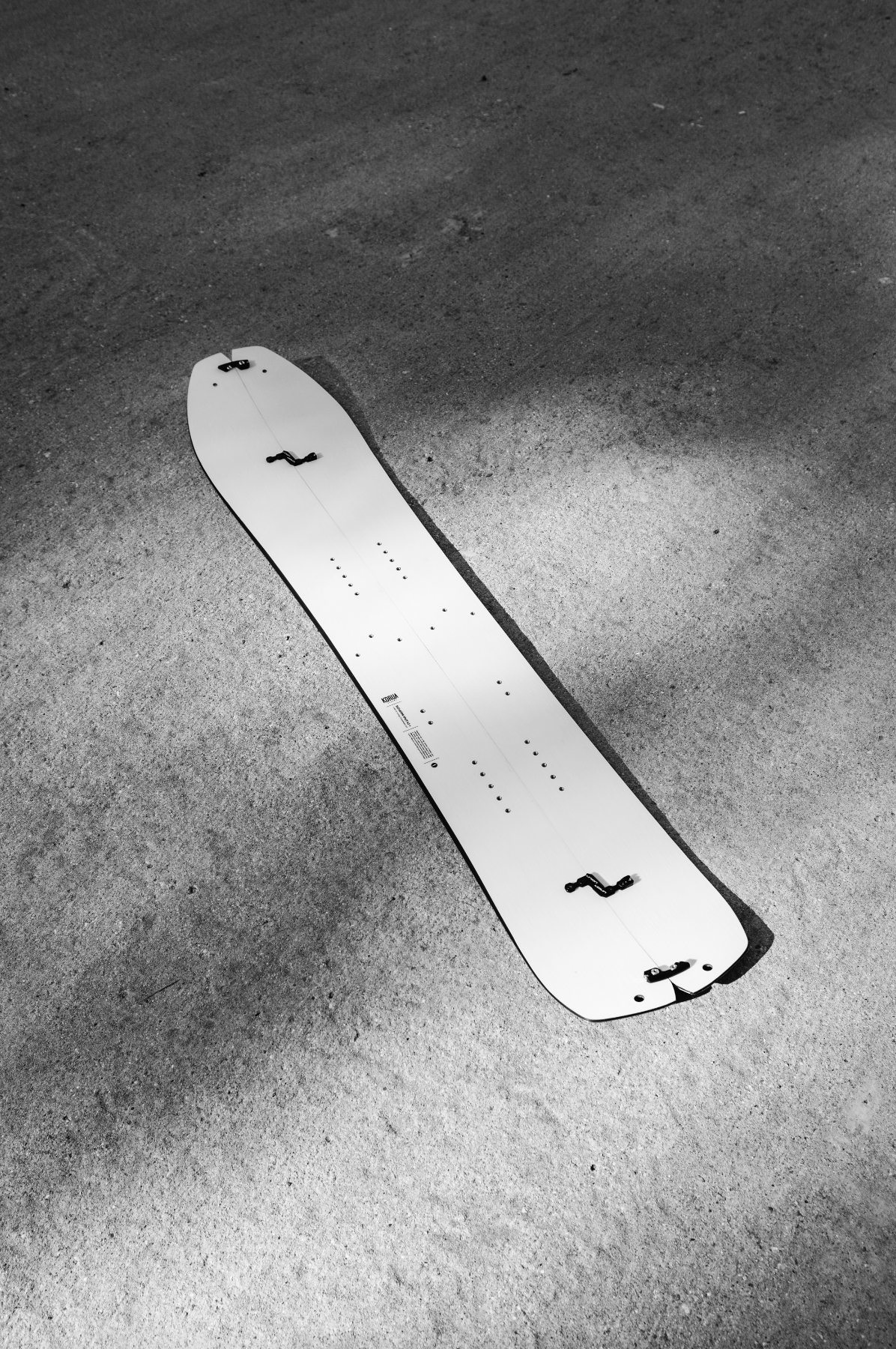 Korua Elevator Split Plus snowboard lying on the snow with a clear view of its design and splitboard features in a snowy landscape.