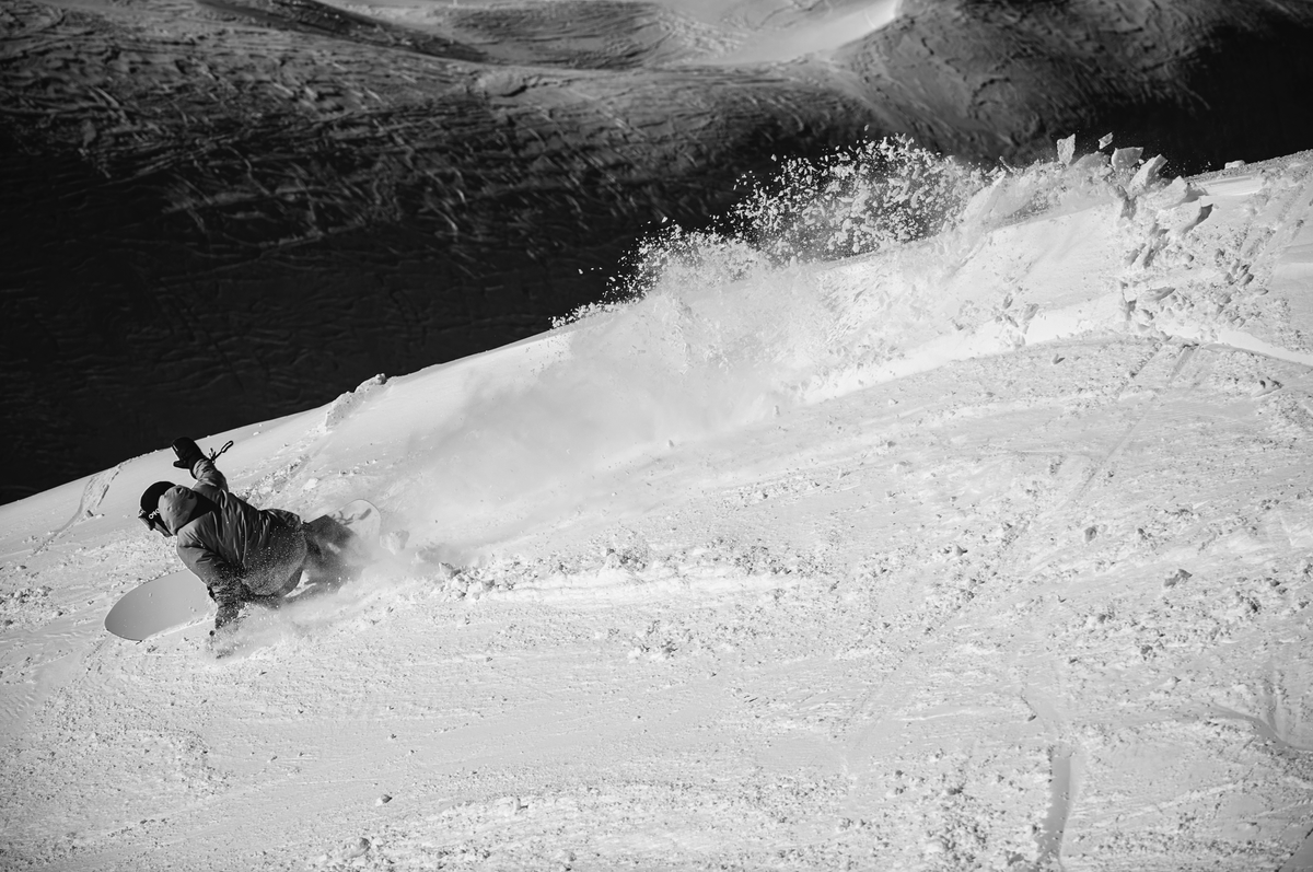 Korua Pin Tonic snowboard shown on heelside carve on groomed snow, highlighting its design and shape for snowboarding.