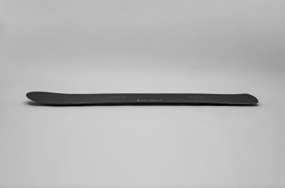 Korua Bullet Train Plus snowboard in snow, side view showcasing its shape and design for versatile winter snowboarding.