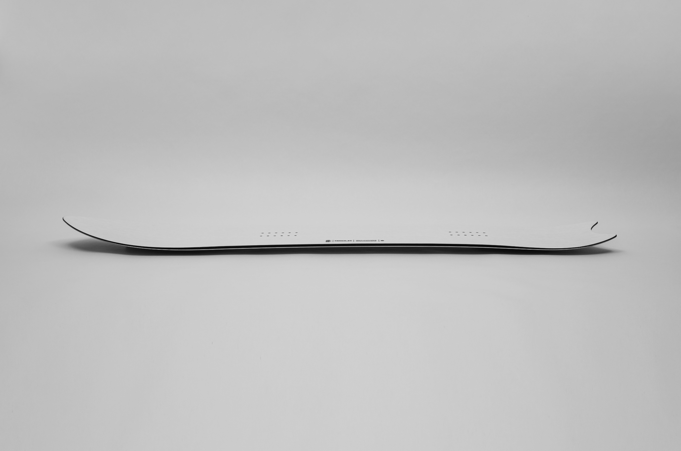 Korua Pencil snowboard in snow, side view showing sleek shape and design, ideal for carving and freestyle snowboarding.