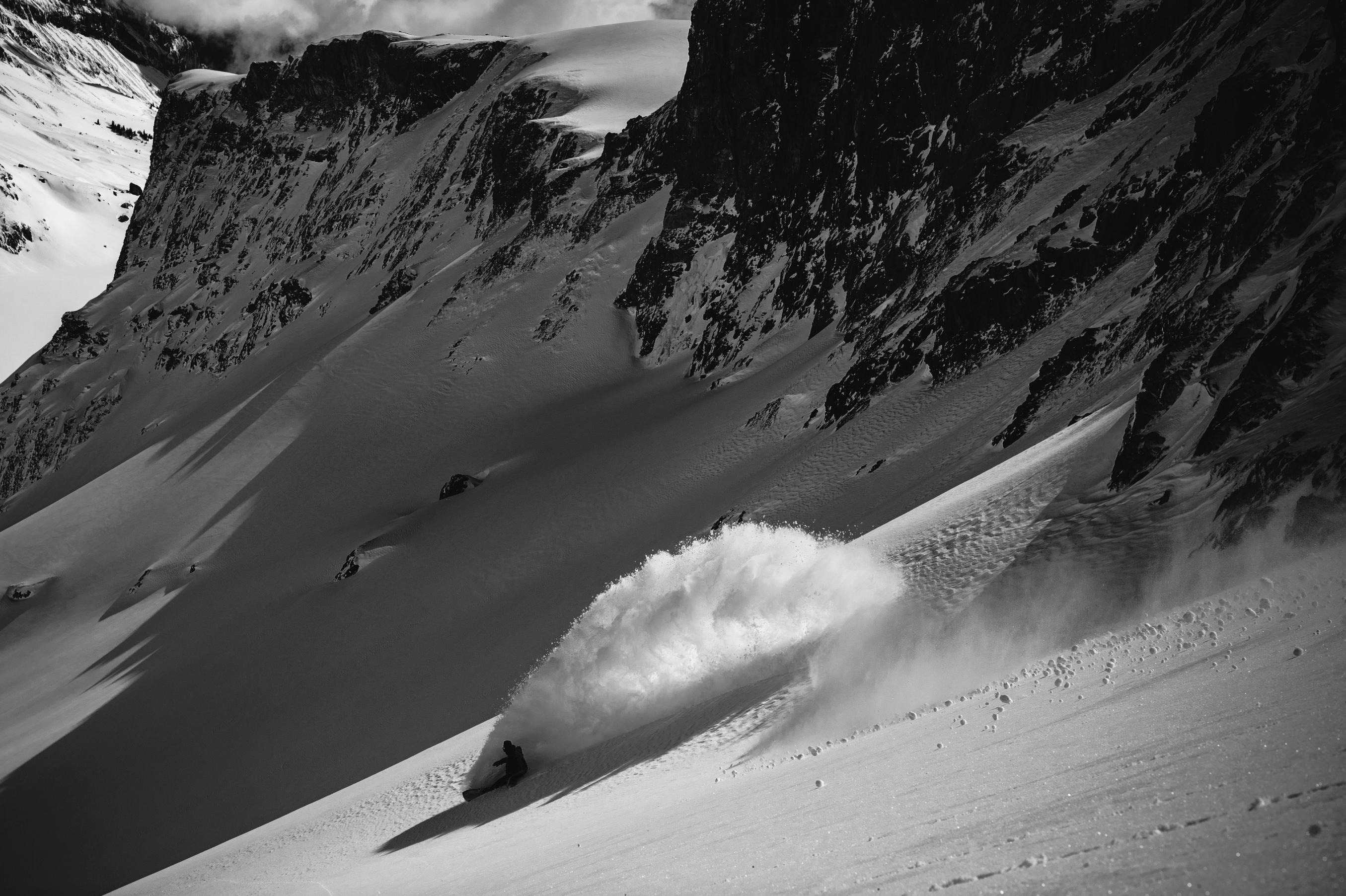 Korua Transition Finder Plus snowboard on snow with scenic mountain backdrop, showcasing its versatile design and vibrant graphics.