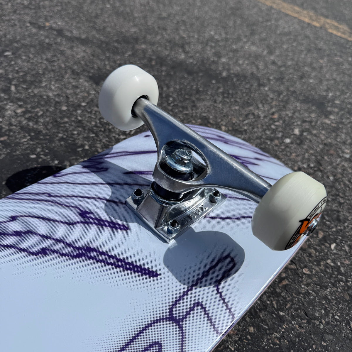 Close-up of the polished silver Krux K5 truck and white OJ wheels on the Milosport Fracture Complete Skateboard.