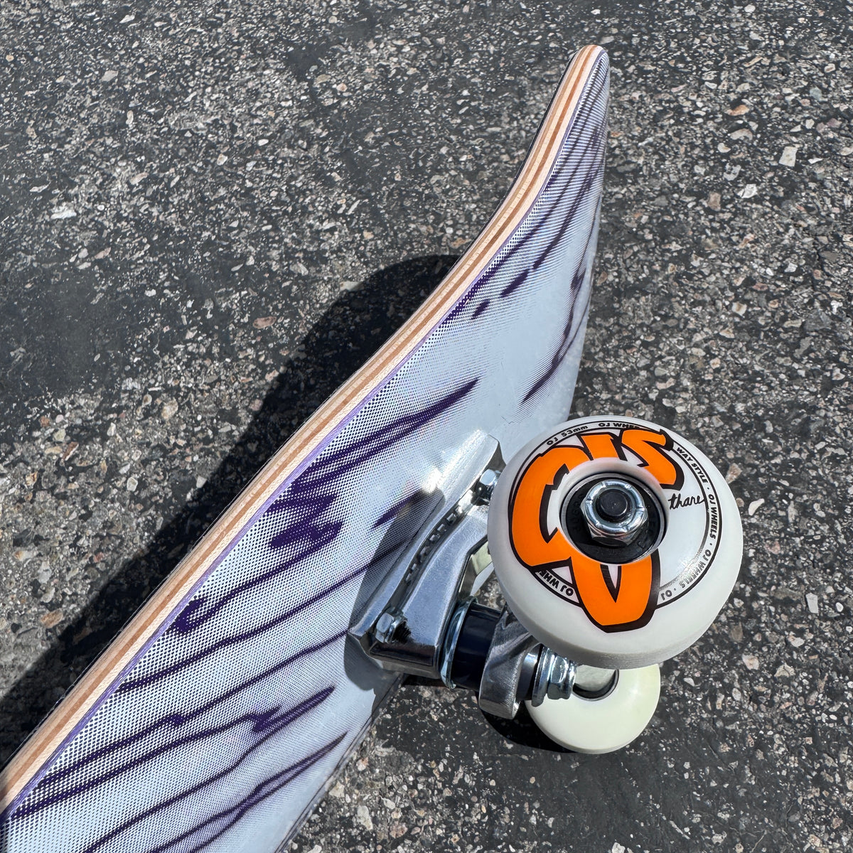 Close-up of the white OJ skateboard wheel, polished Krux truck and layered wood construction on the Milosport Fracture Complete Skateboard.