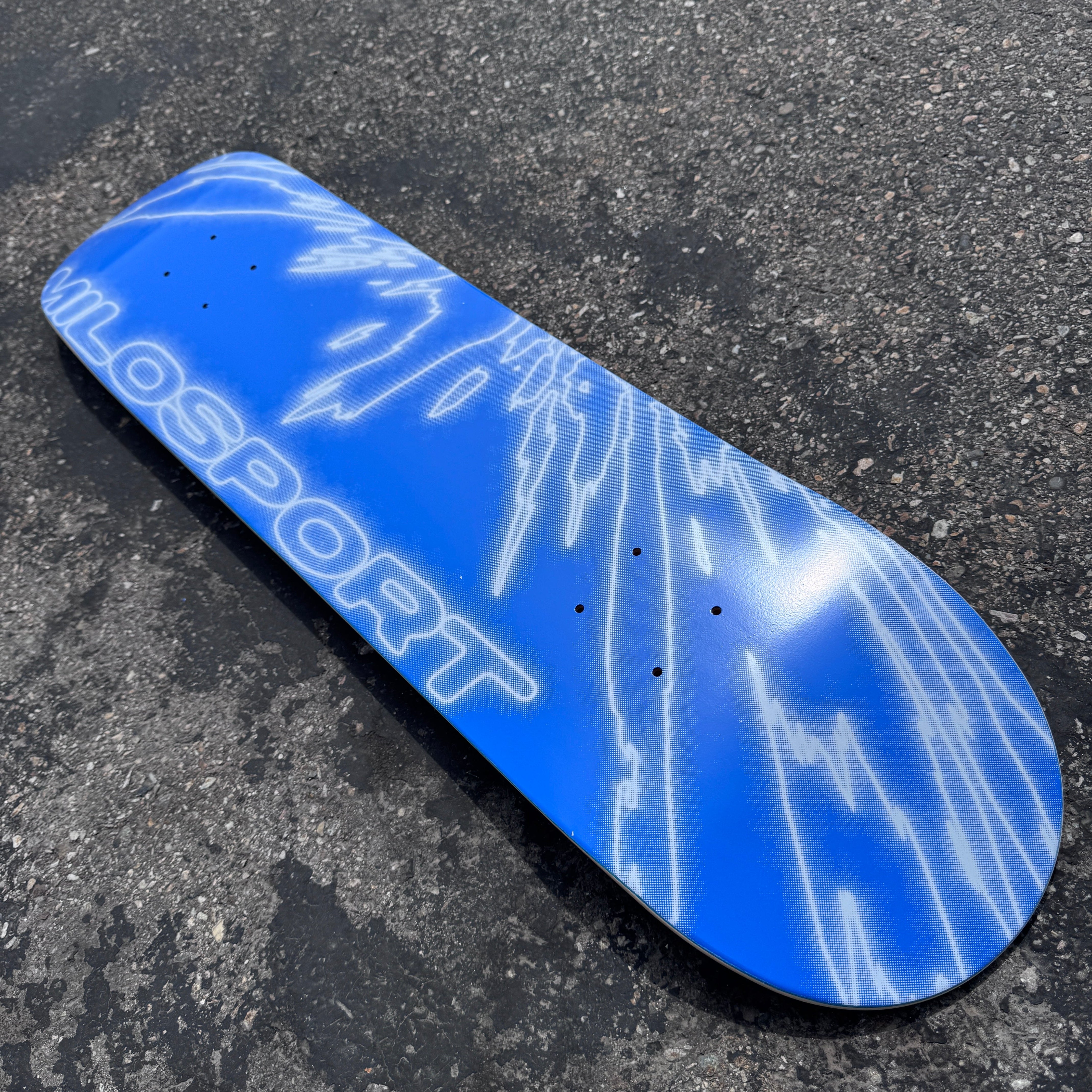 Close-up of the white fractured line artwork and Milosport logo on the blue Fracture skateboard deck.