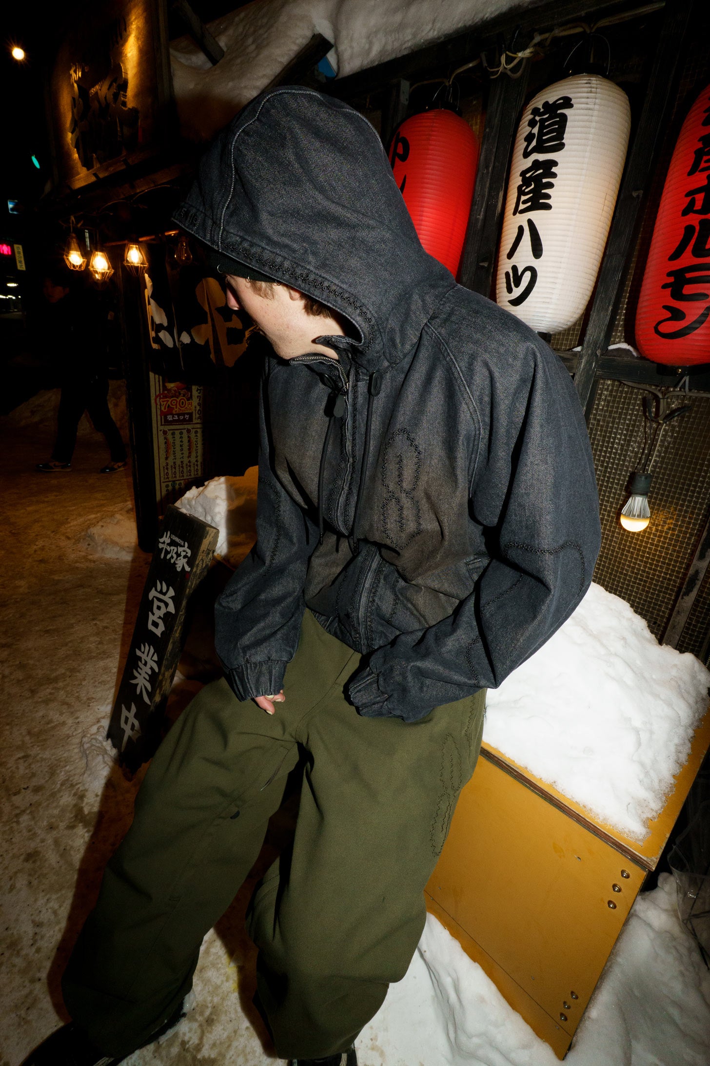 Rider wearing the Souvenir 3 Ply Workwear Pant 2027 in Dark Olive Oxford with a dark hooded jacket in a snowy winter setting.