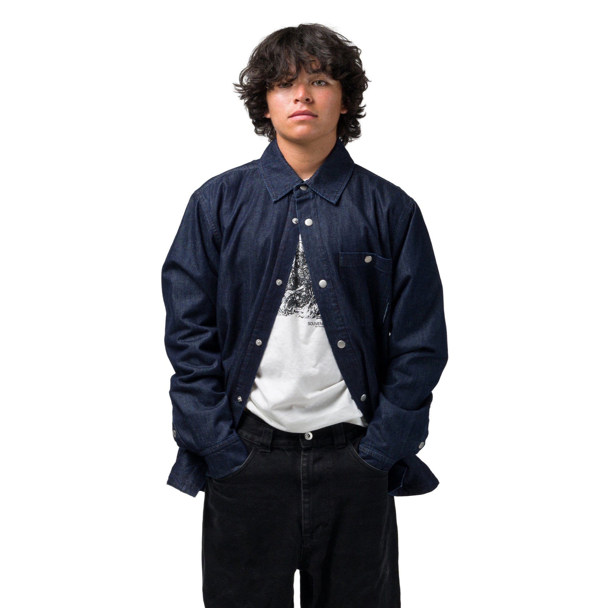 A person wearing a dark navy blue denim overshirt over a white graphic t-shirt and black pants, standing against a solid white background.