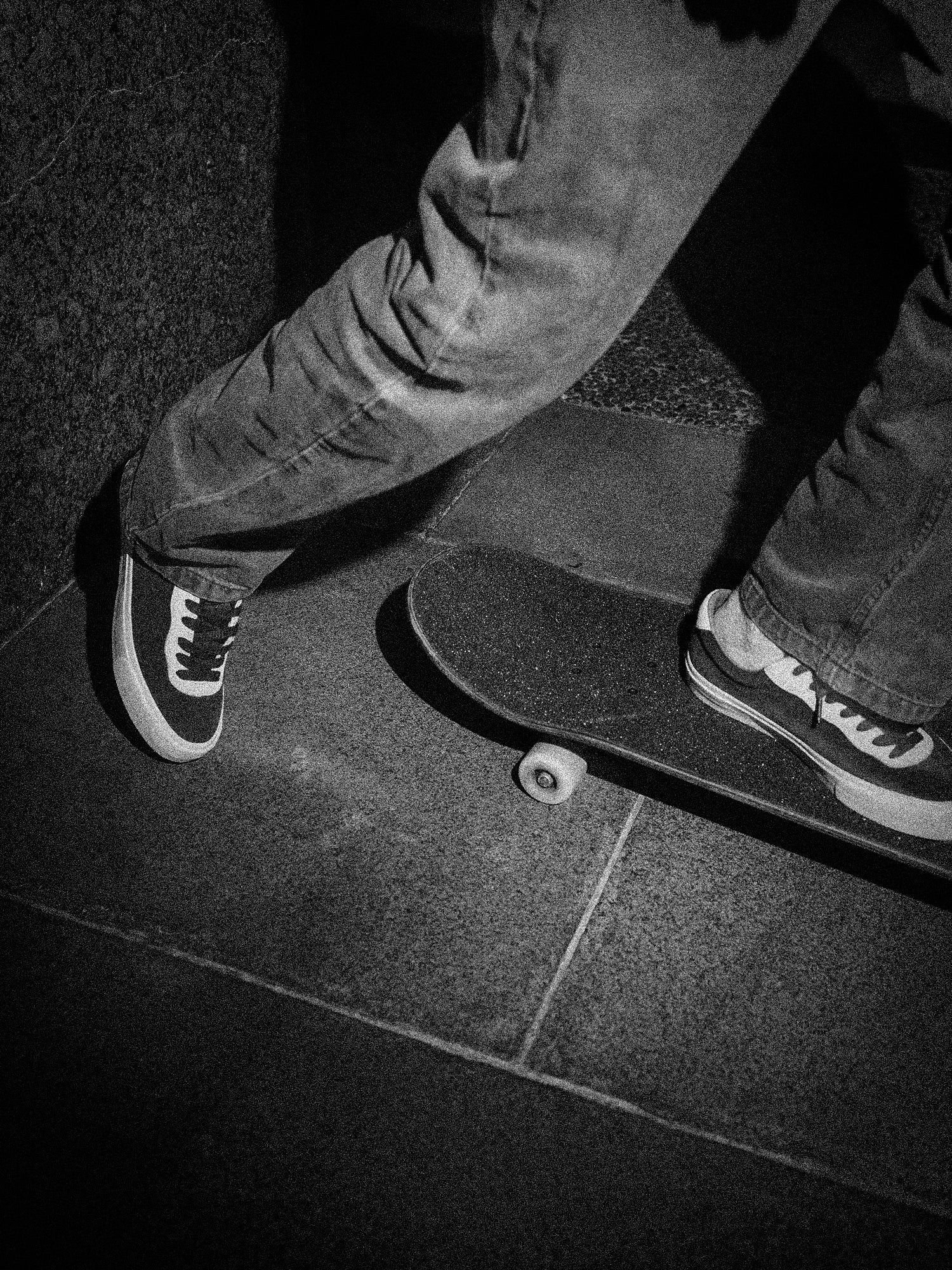 Black and white close-up of a skateboarder wearing skate shoes while standing on a skateboard, used for the Milosport Skate Shoes collection.