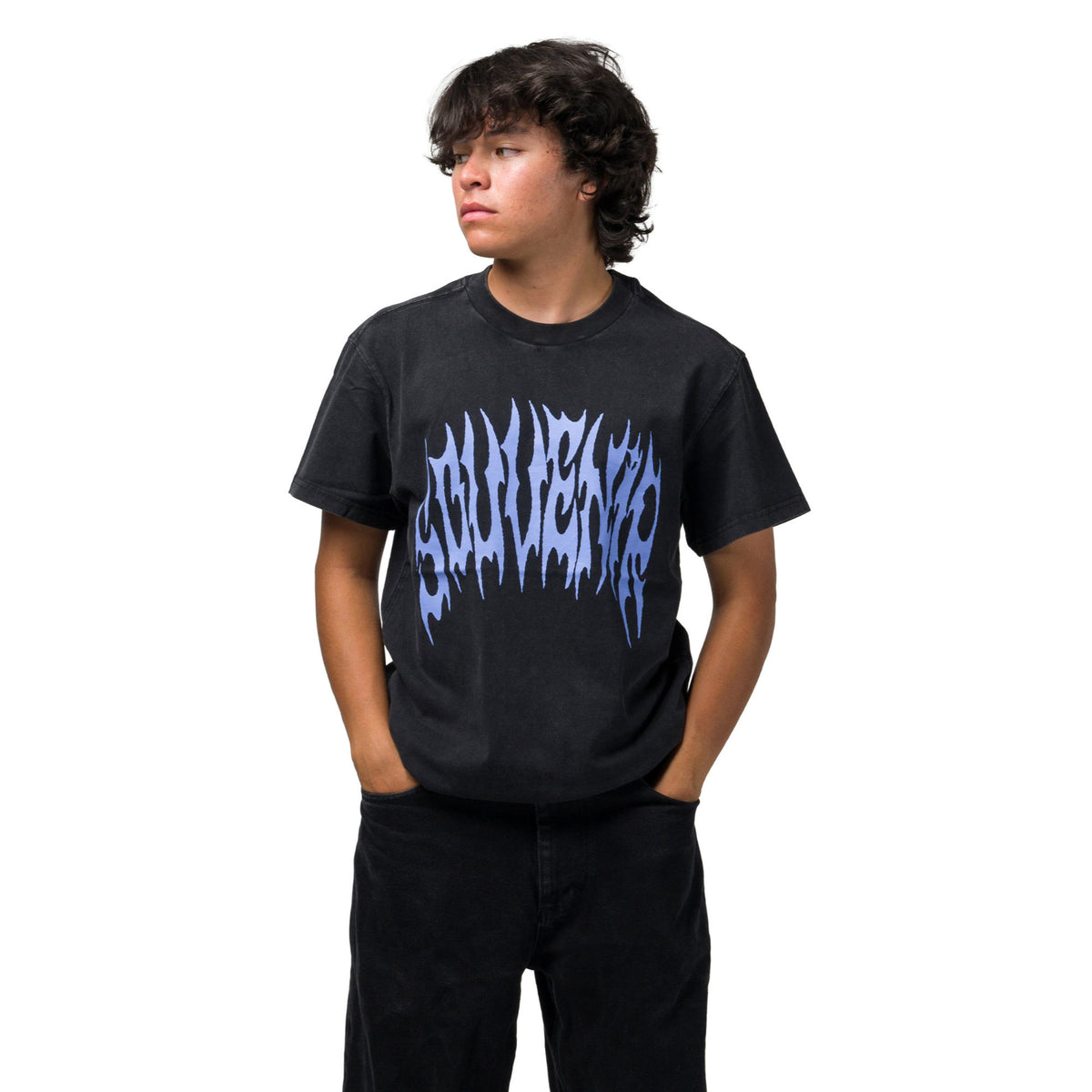 A shredder with dark curly hair wearing a black t-shirt with a blue stylized graphic souvenir logo across the chest, paired with black pants, standing against a solid white background.