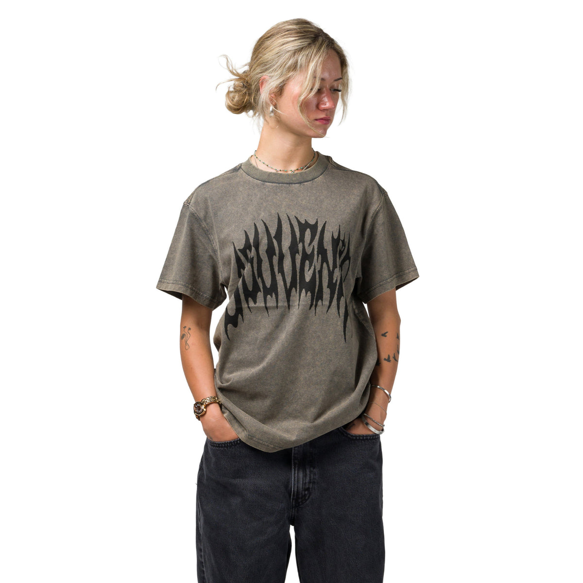 A woman modeling an oversized, faded charcoal gray t-shirt with a black jagged souvenir graphic across the chest, paired with dark jeans, against a plain white background.
