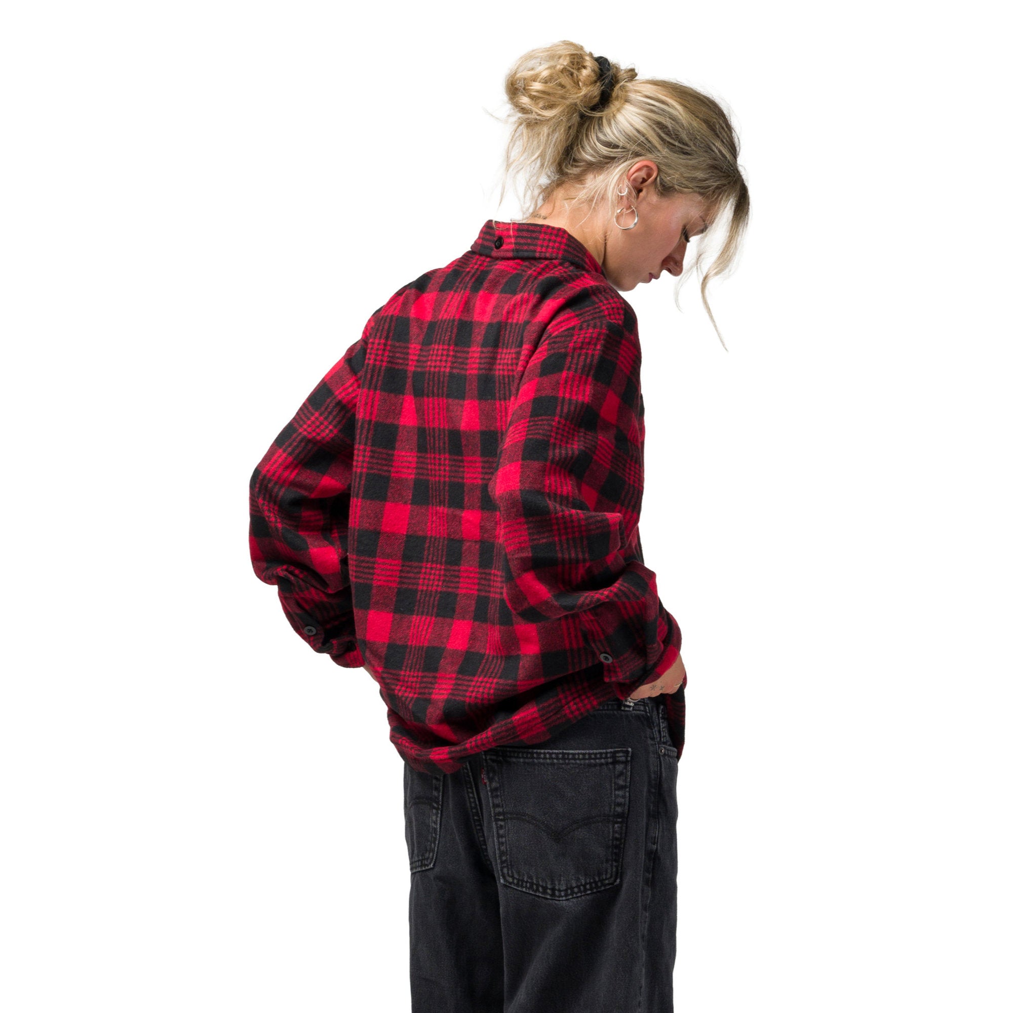 A woman wearing a red and black souvenir plaid flannel shirt, shown from a side-back angle against a solid white background.