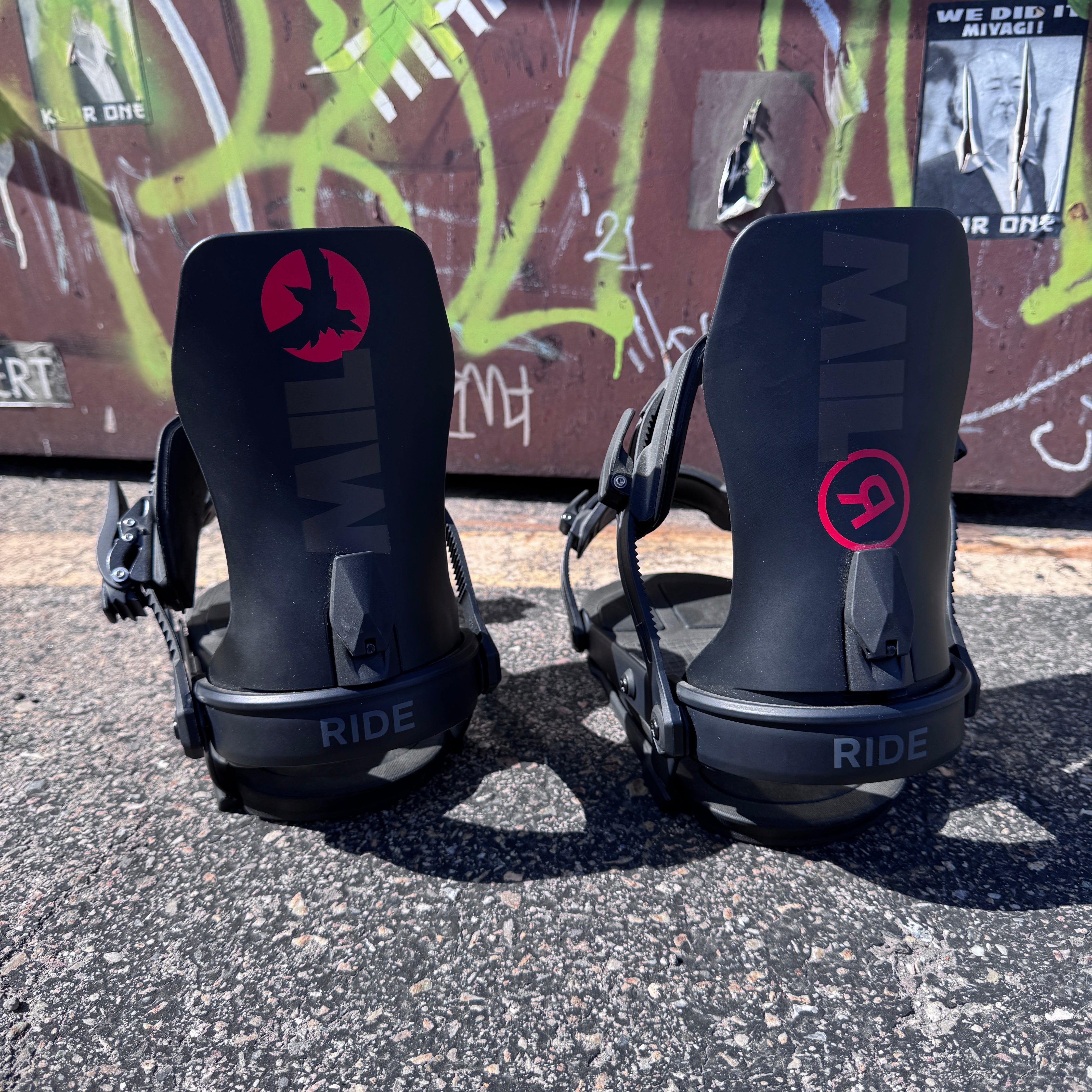 Two black snowboard bindings with 'RIDE' branding on a concrete surface with graffiti in the background.