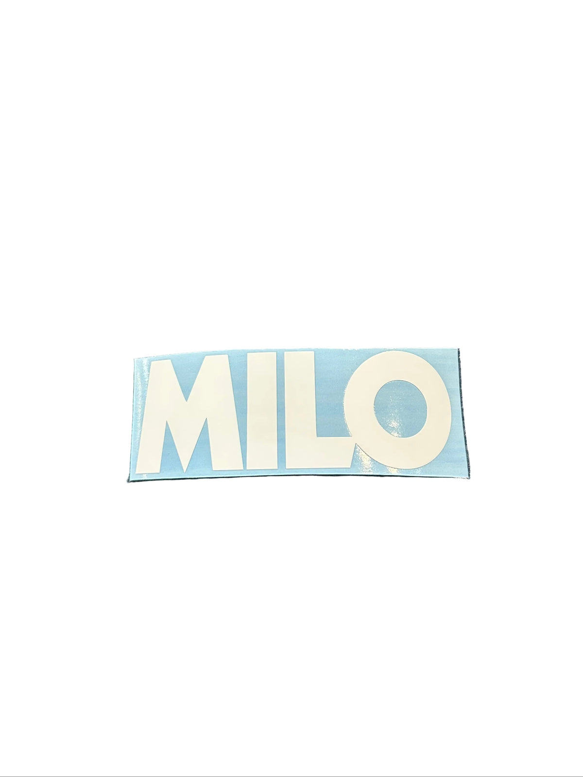 A rectangular blue and white sticker with the word 'MILO' in white letters on a blue background, placed on a dark textured surface with red lettering in the background.