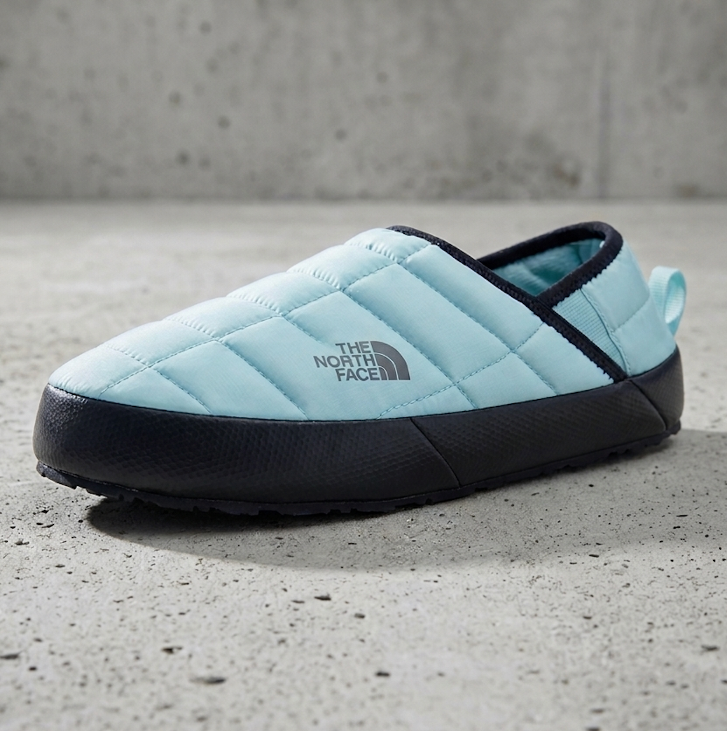 A light blue quilted slip-on shoe by The North Face with a black sole and trim, photographed on a textured gray concrete surface.