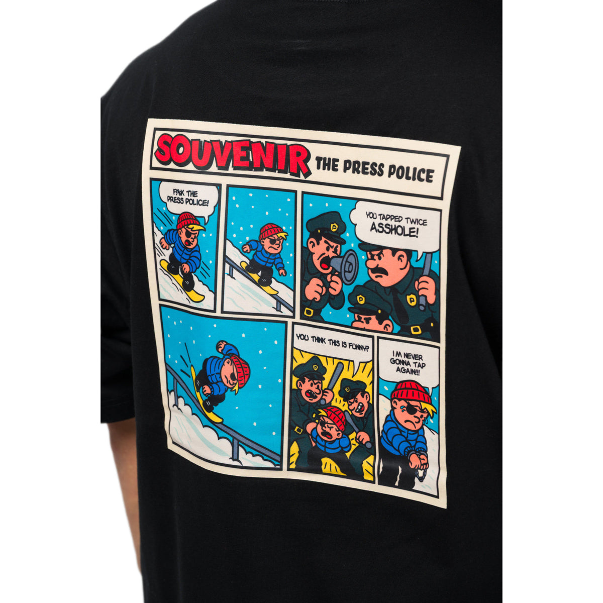 A black short-sleeve t-shirt featuring a large vintage comic strip graphic on the back. The graphic is titled 'SOUVENIR THE PRESS POLICE' and shows a cartoon reporter in a red hat reporting from the snow, with panels containing speech bubbles and a police officer.