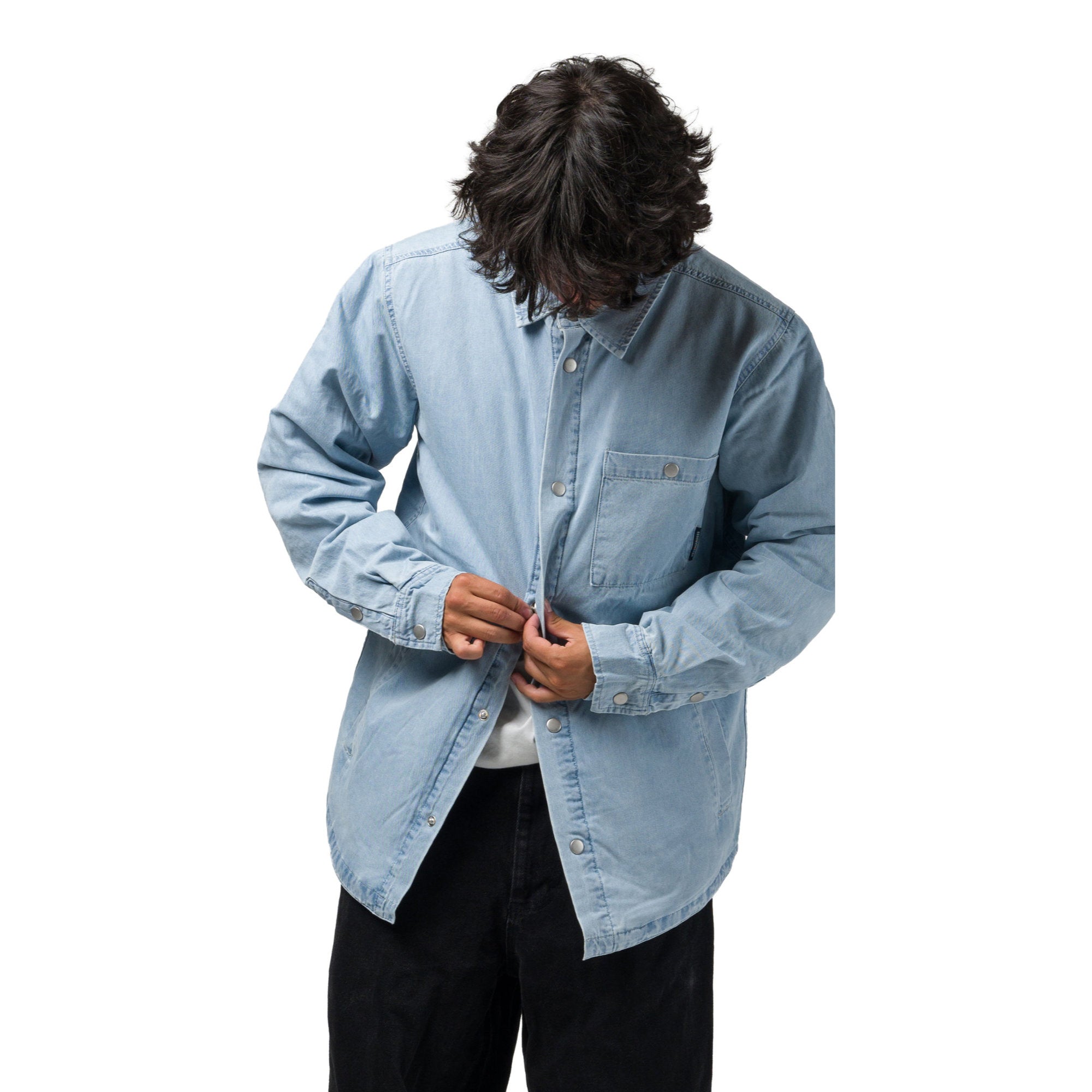 A model wearing a light blue souvenir denim button-up shirt over a white undershirt and black pants, shown from the waist up against a solid white background.