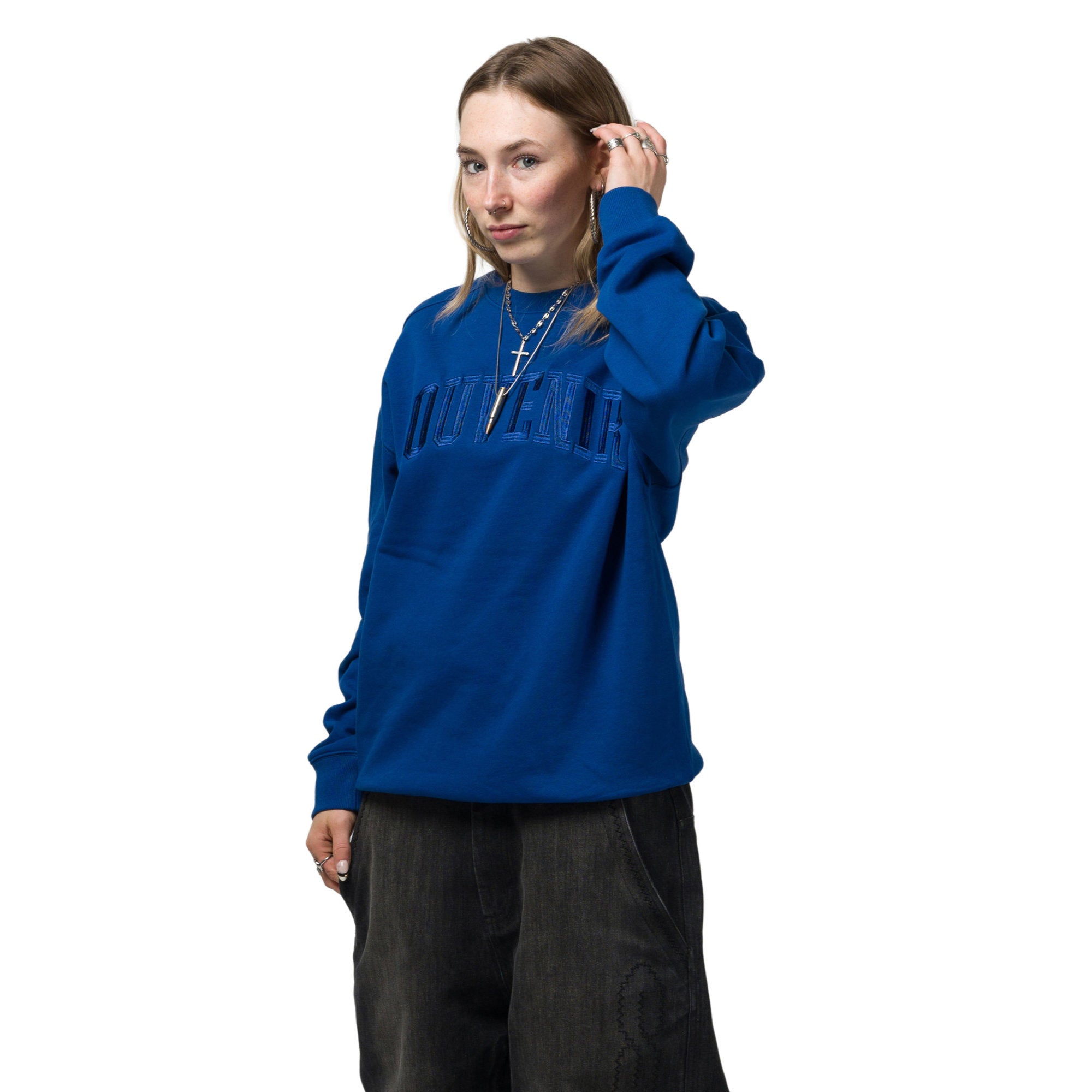 A woman modeling a royal blue crewneck sweatshirt with 'UNIVERSITY' printed across the chest in a tonal, slightly textured font, paired with dark gray wide-leg jeans against a solid white background.