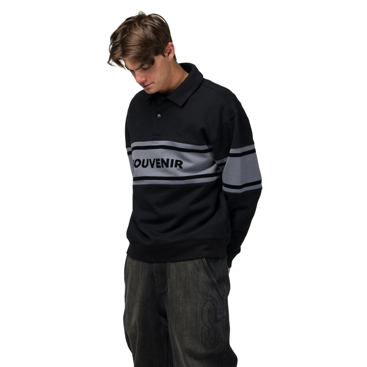 A man wearing a black long-sleeve knit polo sweater with a gray horizontal stripe across the chest and sleeves, featuring the word 'Mouvénir' printed on the chest, set against a plain white background.