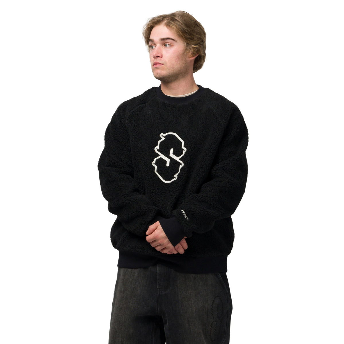A man wearing a black sherpa fleece crewneck sweatshirt with a white outlined graphic logo on the chest, paired with dark gray jeans, photographed against a solid white background.