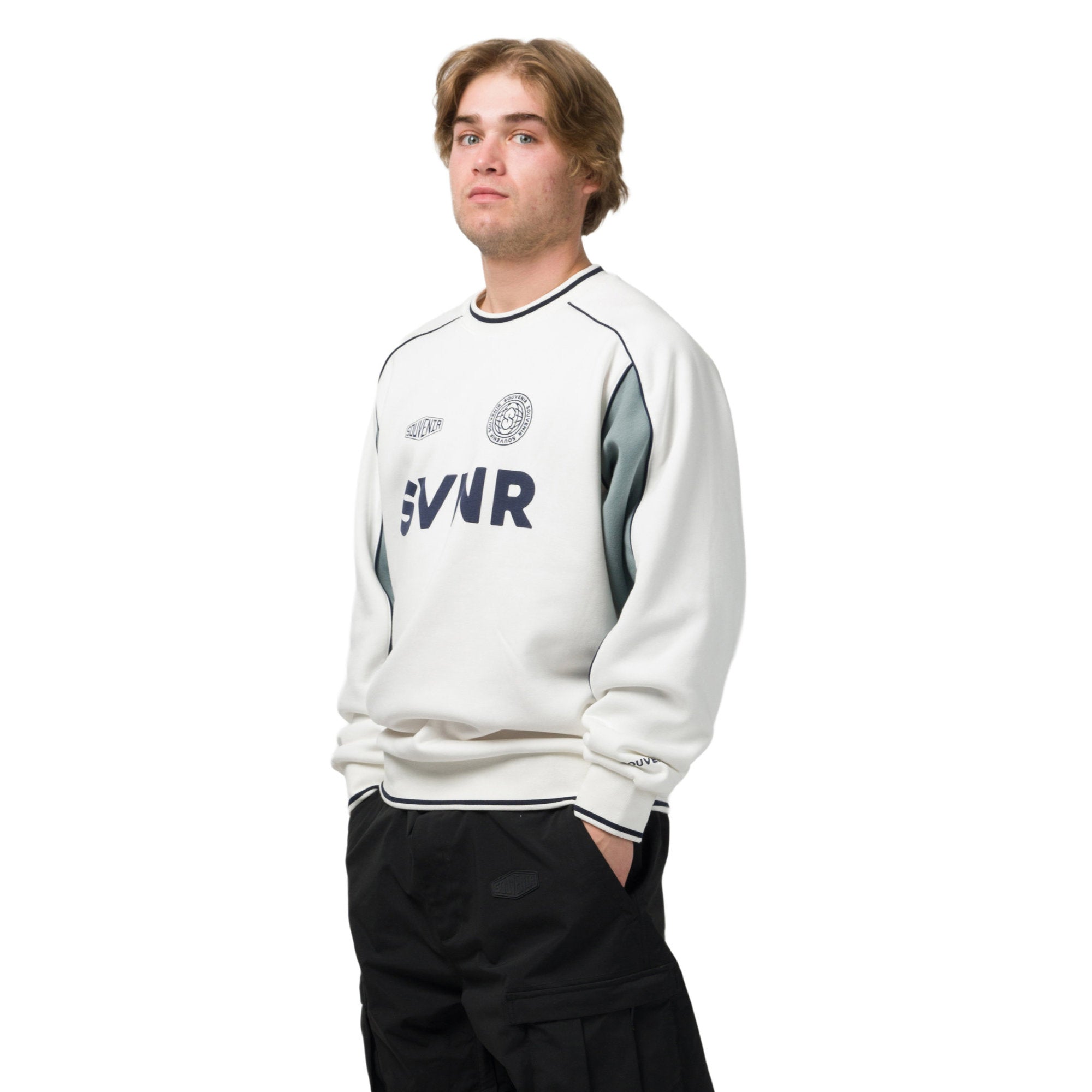 A man wearing a white crewneck sweatshirt with gray side panels and navy blue 'SVIR' lettering on the chest, paired with black cargo pants, against a plain white background.