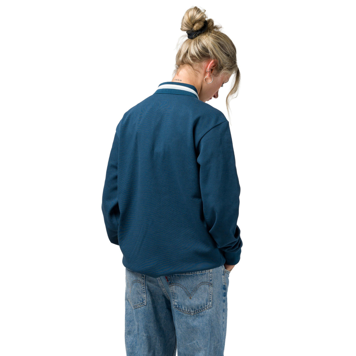 A woman viewed from behind wearing a navy blue souvenir sweater with a white and navy striped collar, paired with light-wash blue jeans, against a plain white background.