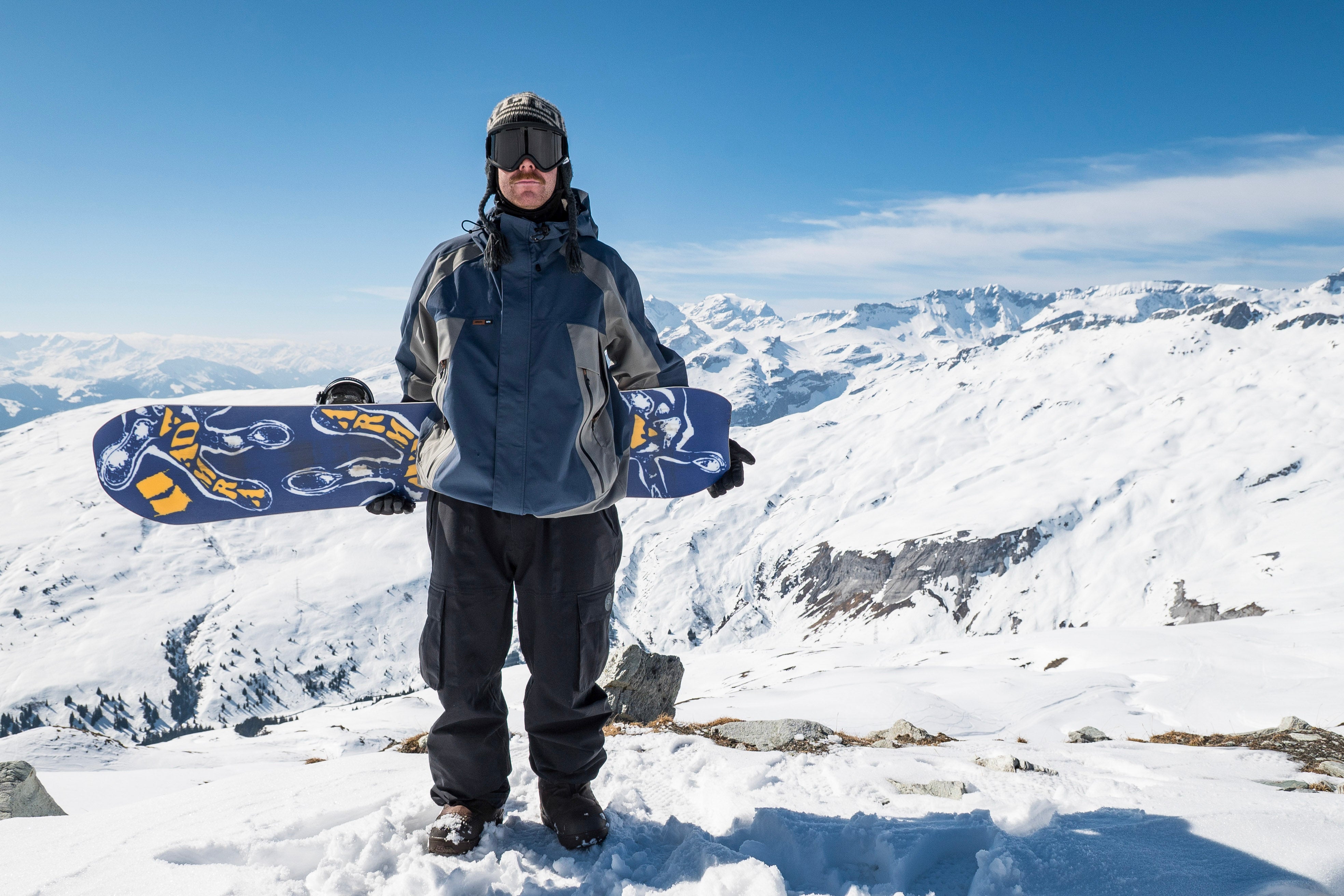 Armada Sicko Snowboard 2027 with Alek standing on snowy terrain, showcasing the board's design and construction.