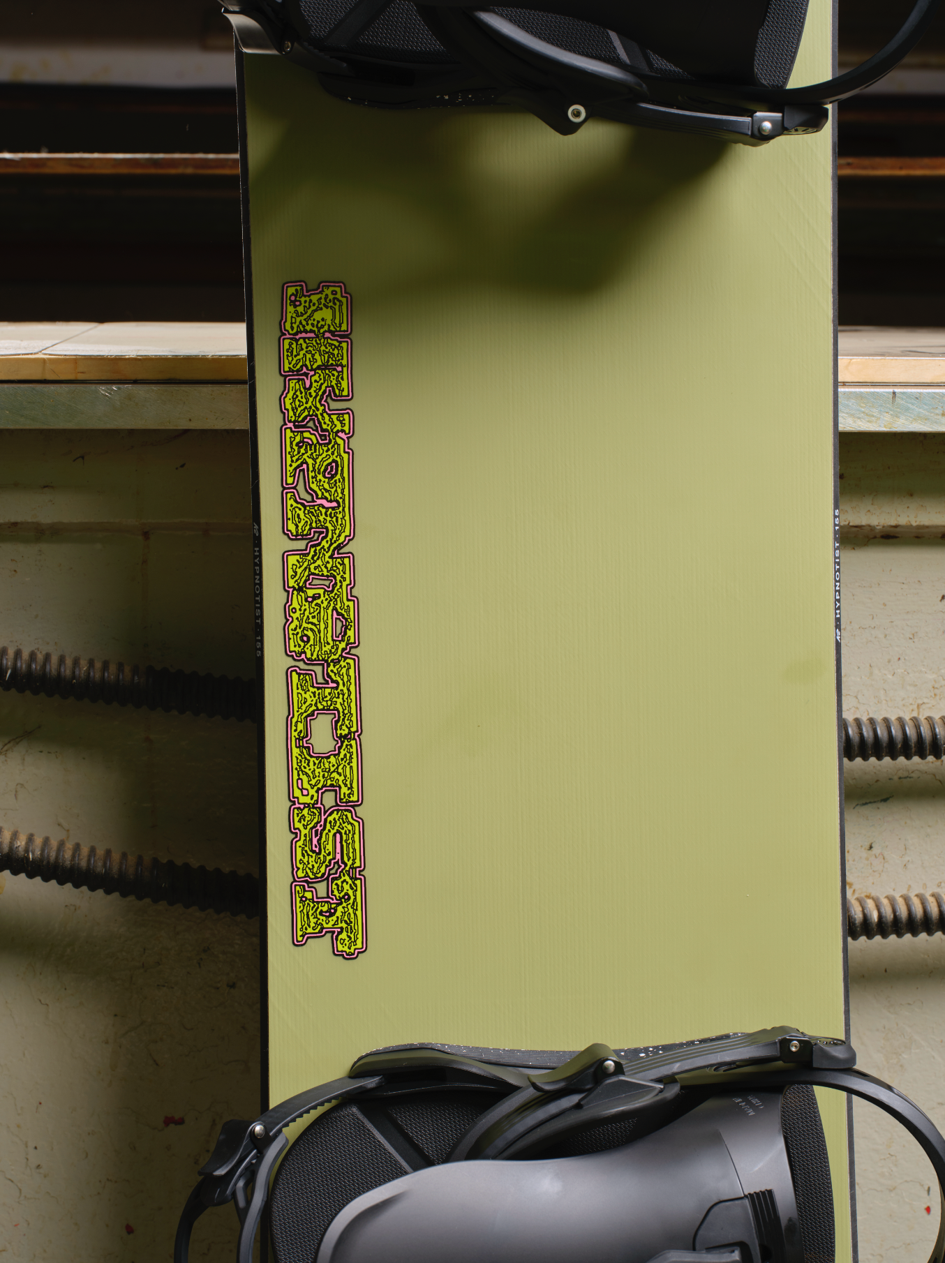 K2 Hypnotist snowboard for snowboarding, featuring a center workshop design with colorful graphics on the top surface.