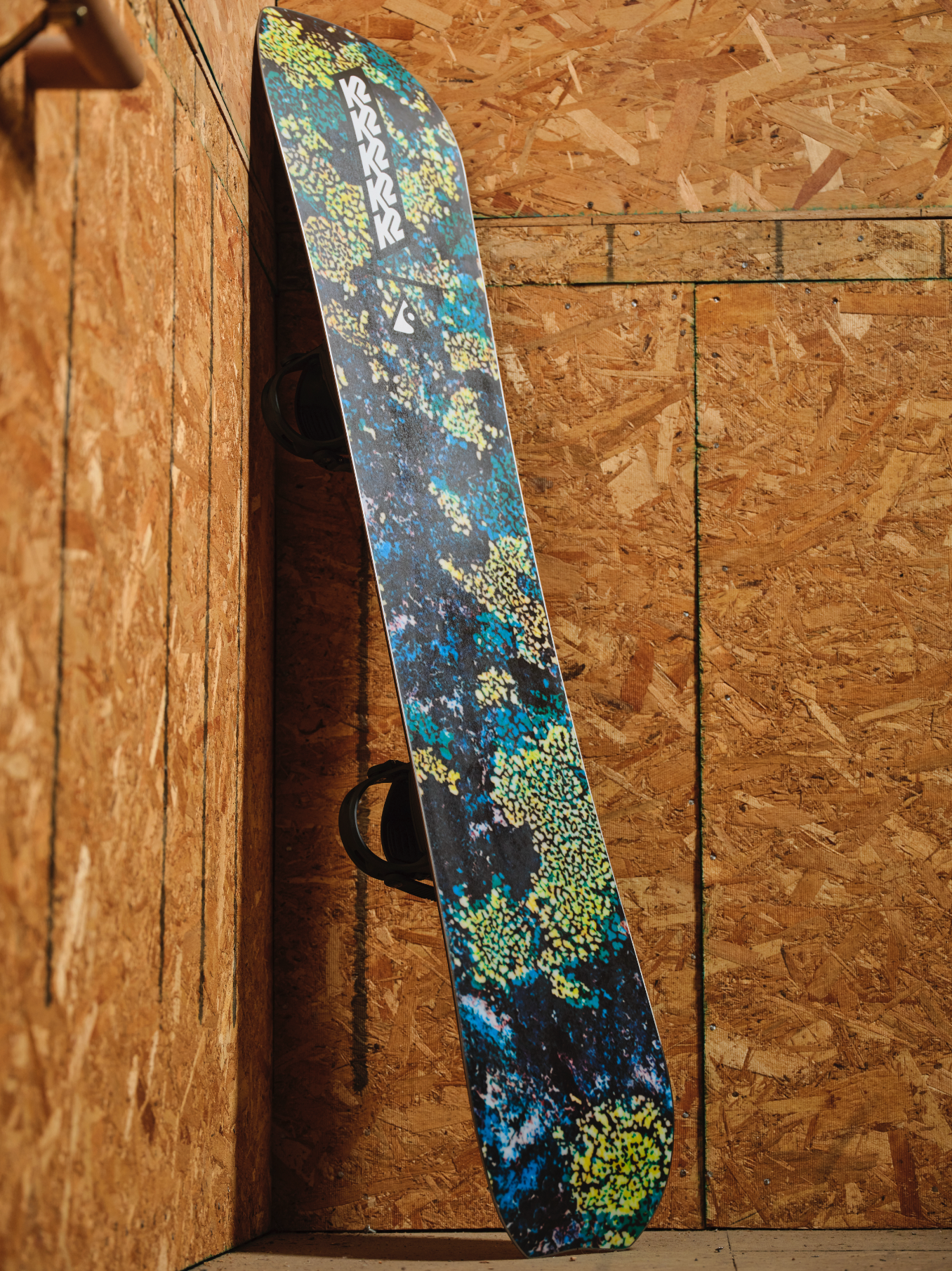 K2 Passport Jr snowboard for kids, showing the base and ply design on a winter snow background.