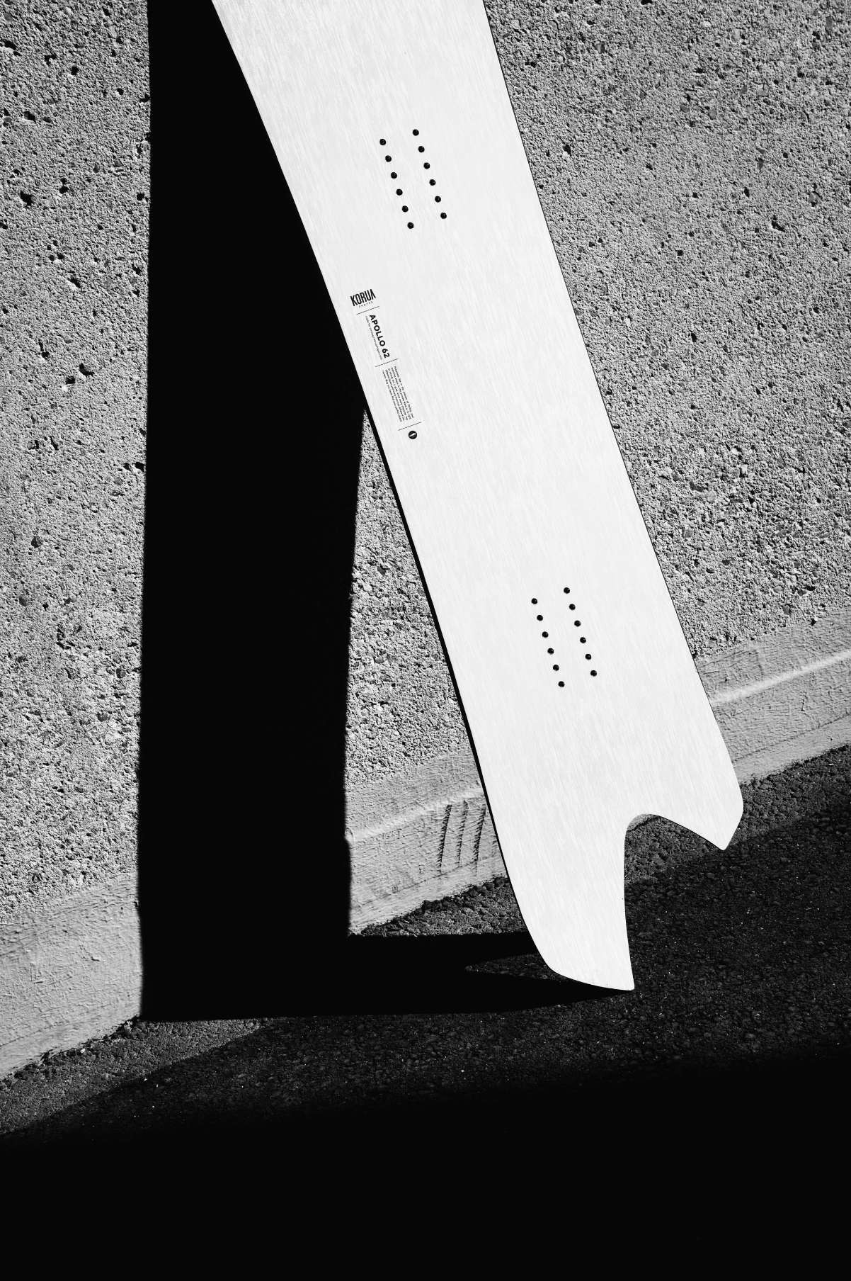 Korua Apollo snowboarding snowboard with tail against cement wall, showcasing its design and structure for snow sports enthusiasts.