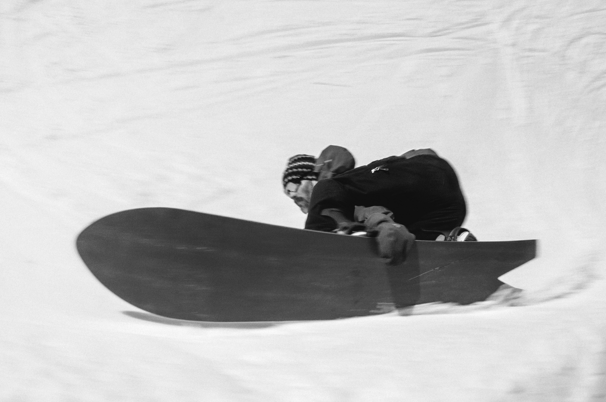 Korua Dart snowboard with Nicholas performing a toeside grab on snow, showcasing the board's design and rider's skill.