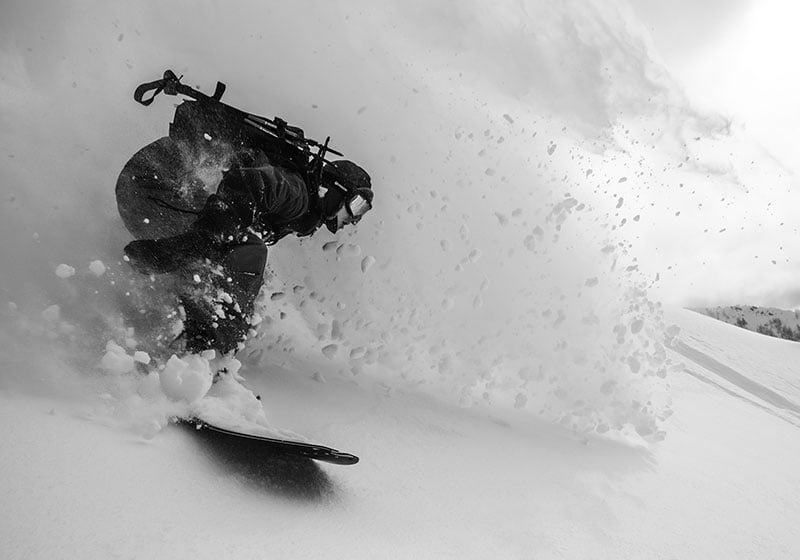 Korua Elevator Split Plus snowboard on snow with a skier making turns, showcasing the snowboard's design and performance in winter conditions.