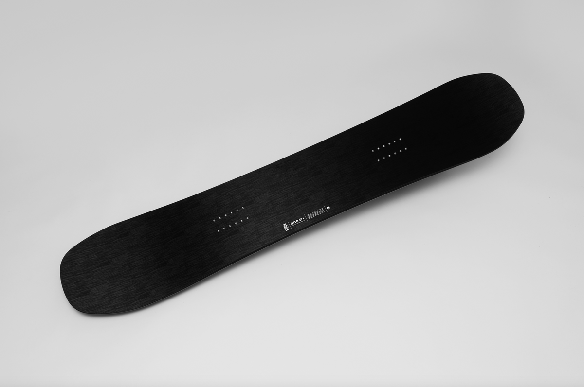 Korua Otto Plus snowboard lying on snow, showcasing its design and shape in a winter studio setting.