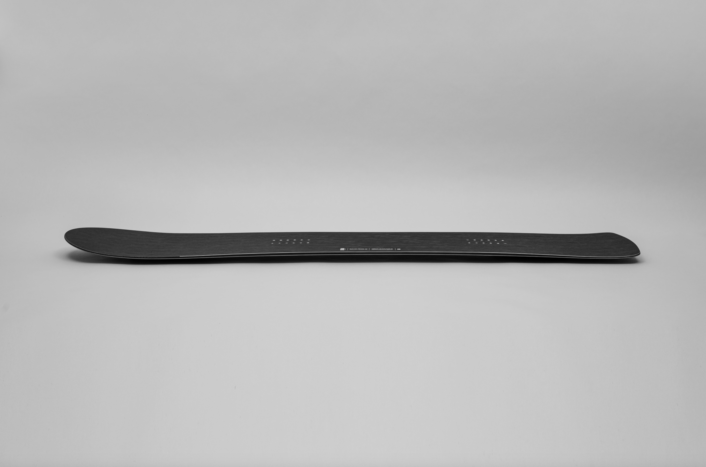 Korua Bullet Train Plus snowboard in snow, side view showcasing its shape and design for versatile winter snowboarding.