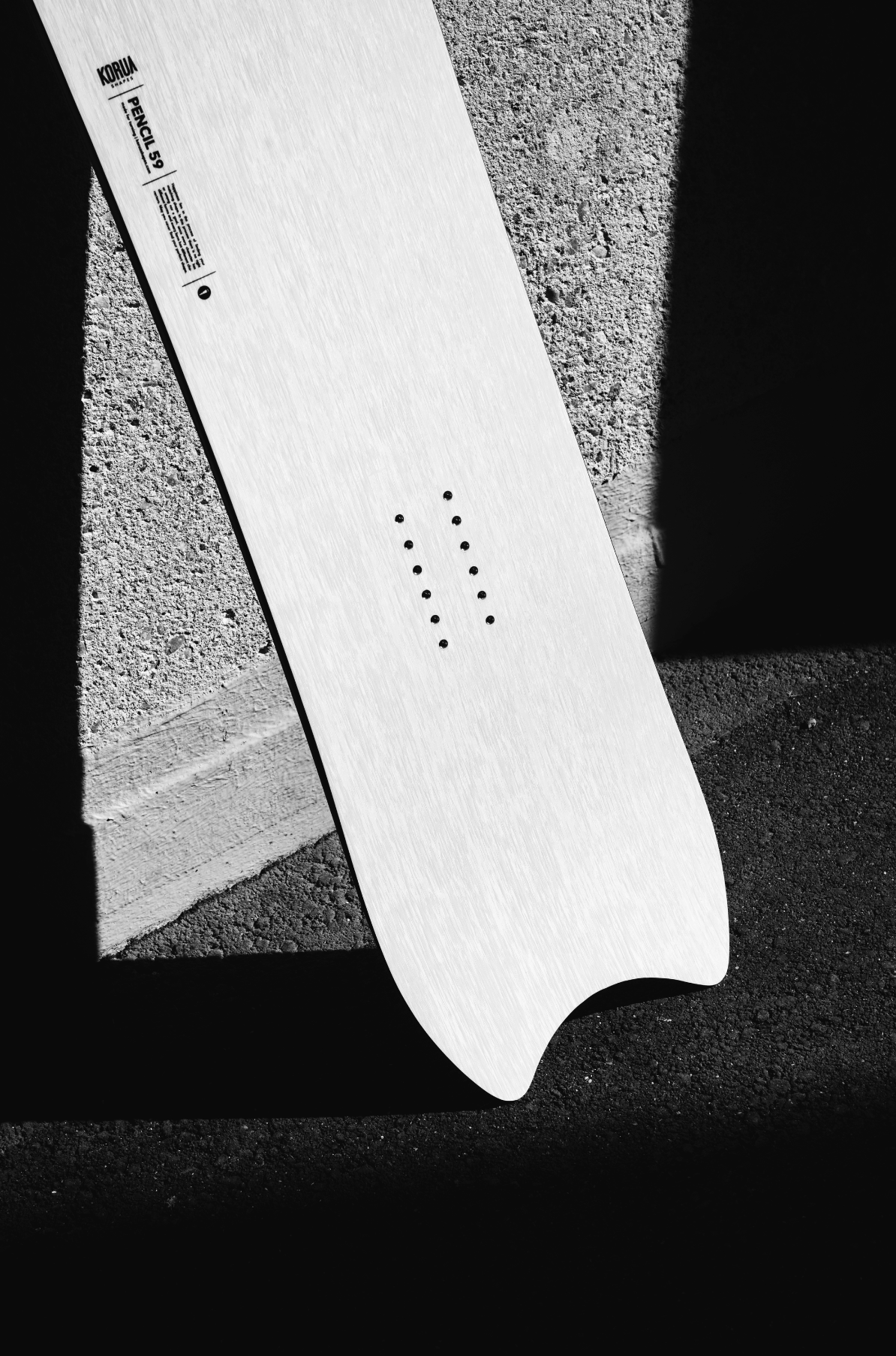 Korua Pencil Junior snowboard with distinctive shape, featuring a tapered tail and wood finish, designed for versatile snowboarding.
