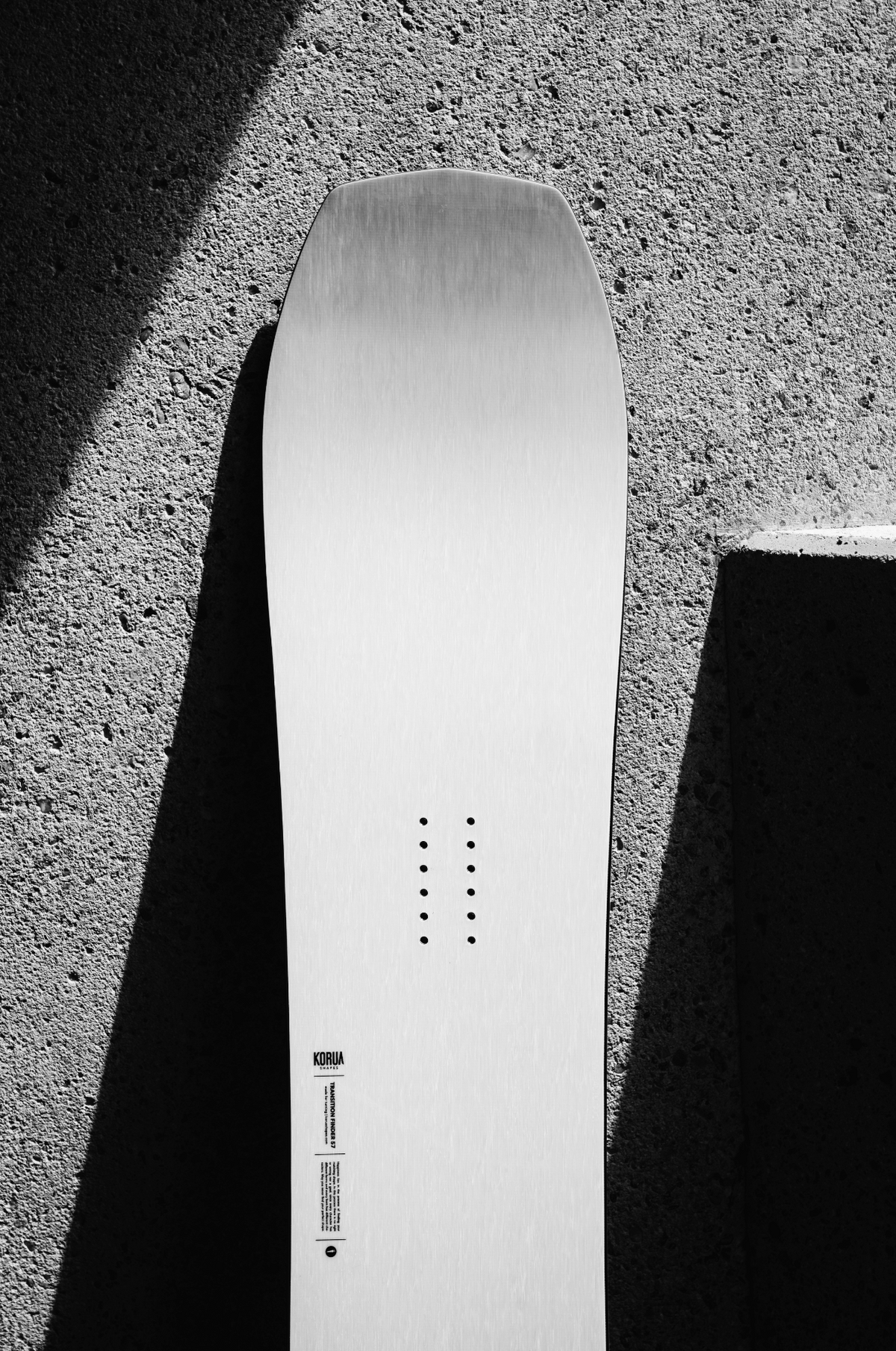 Korua Transition Finder snowboard outdoors, showing the nose design on a cement background