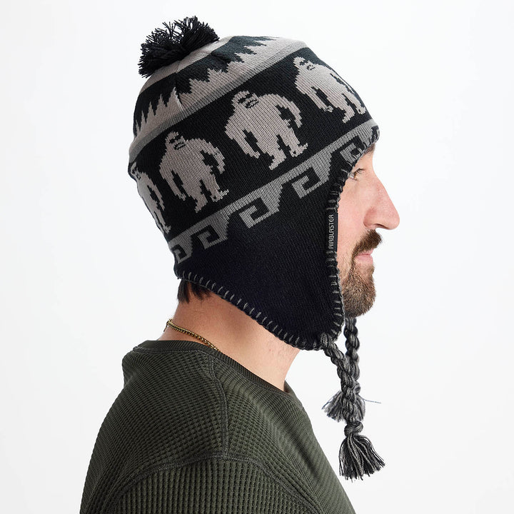 Side view of the Airblaster Squatchamama Beanie 2027 in Charcoal showing the pom top, ear flap, braided tassel and Sasquatch knit pattern.