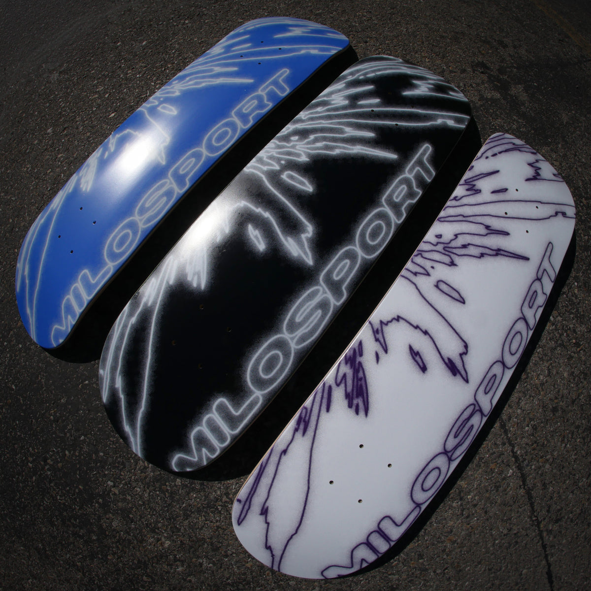 Three Milosport Elbow Fracture skateboard decks in blue and white, black and white, and white and purple displayed outdoors on pavement.