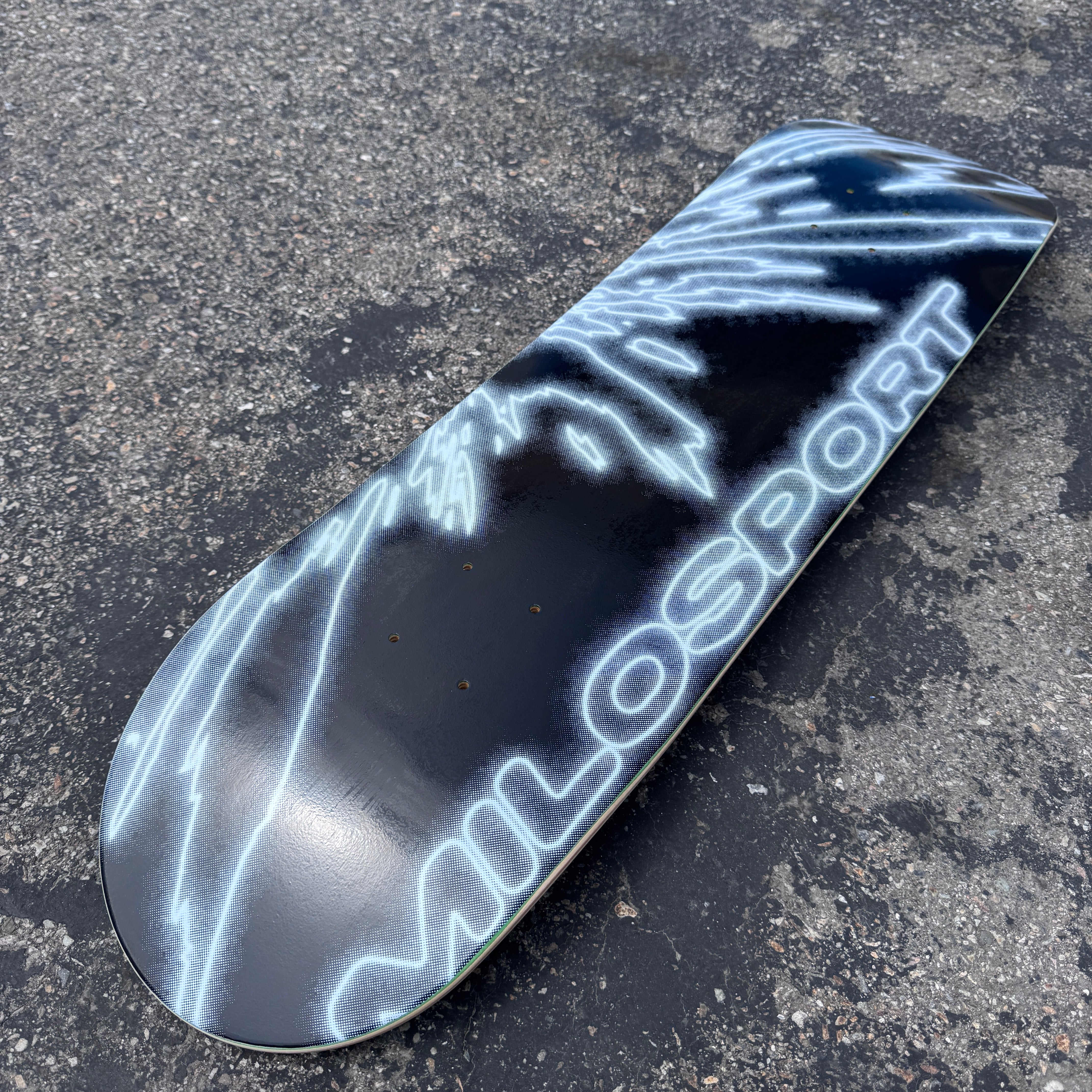 Angled outdoor view of the black and white Milosport Fracture skateboard deck showing the full fractured graphic and popsicle shape.