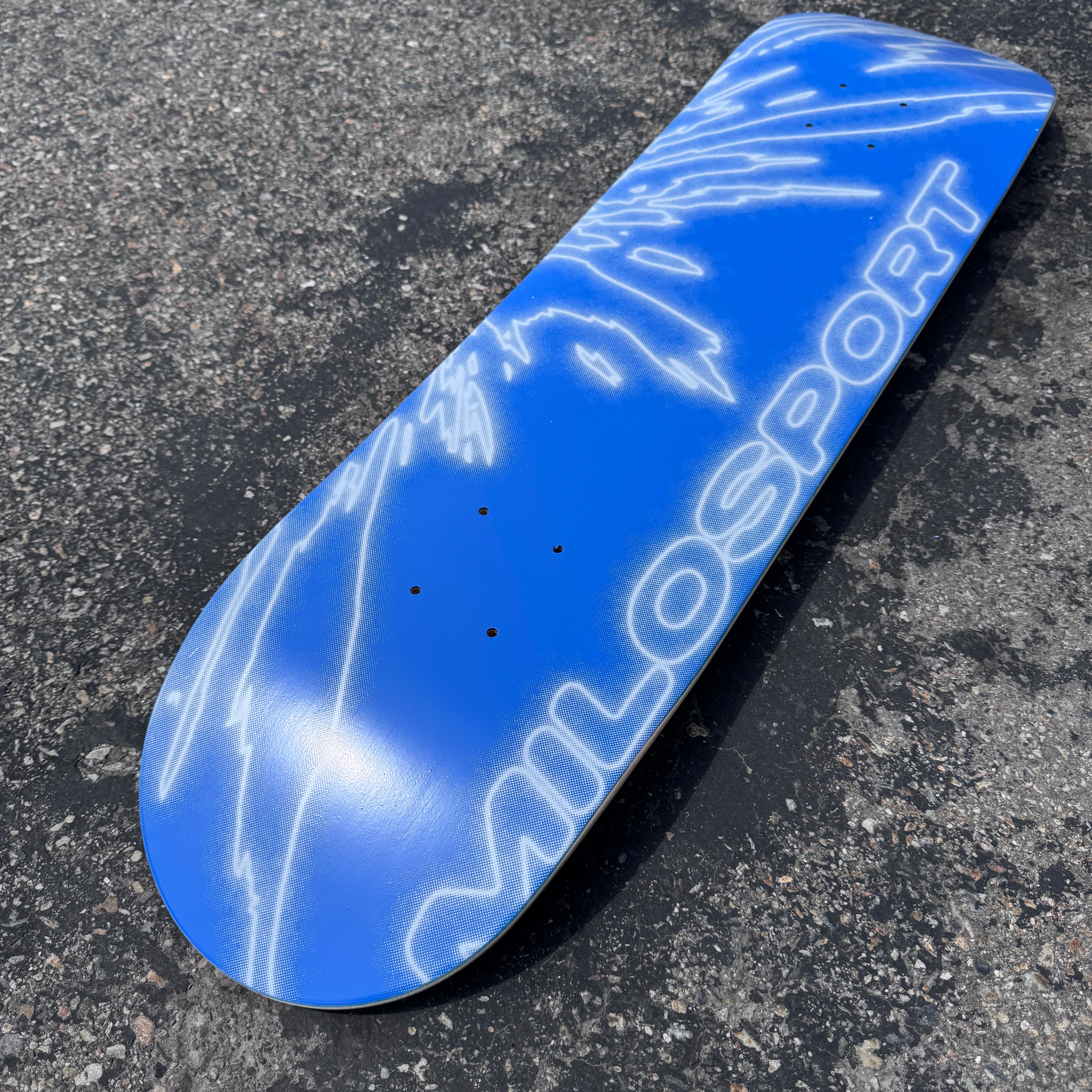 Angled outdoor view of the blue and white Milosport Fracture skateboard deck showing the full fractured graphic and popsicle shape.