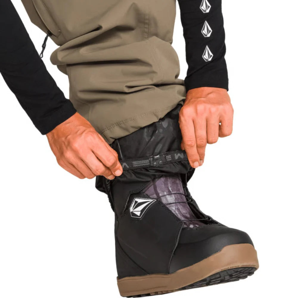 Close-up of the Volcom Liftline 20K Pant 2027 in Teak showing the stretch boot gaiter pulled over a snowboard boot.