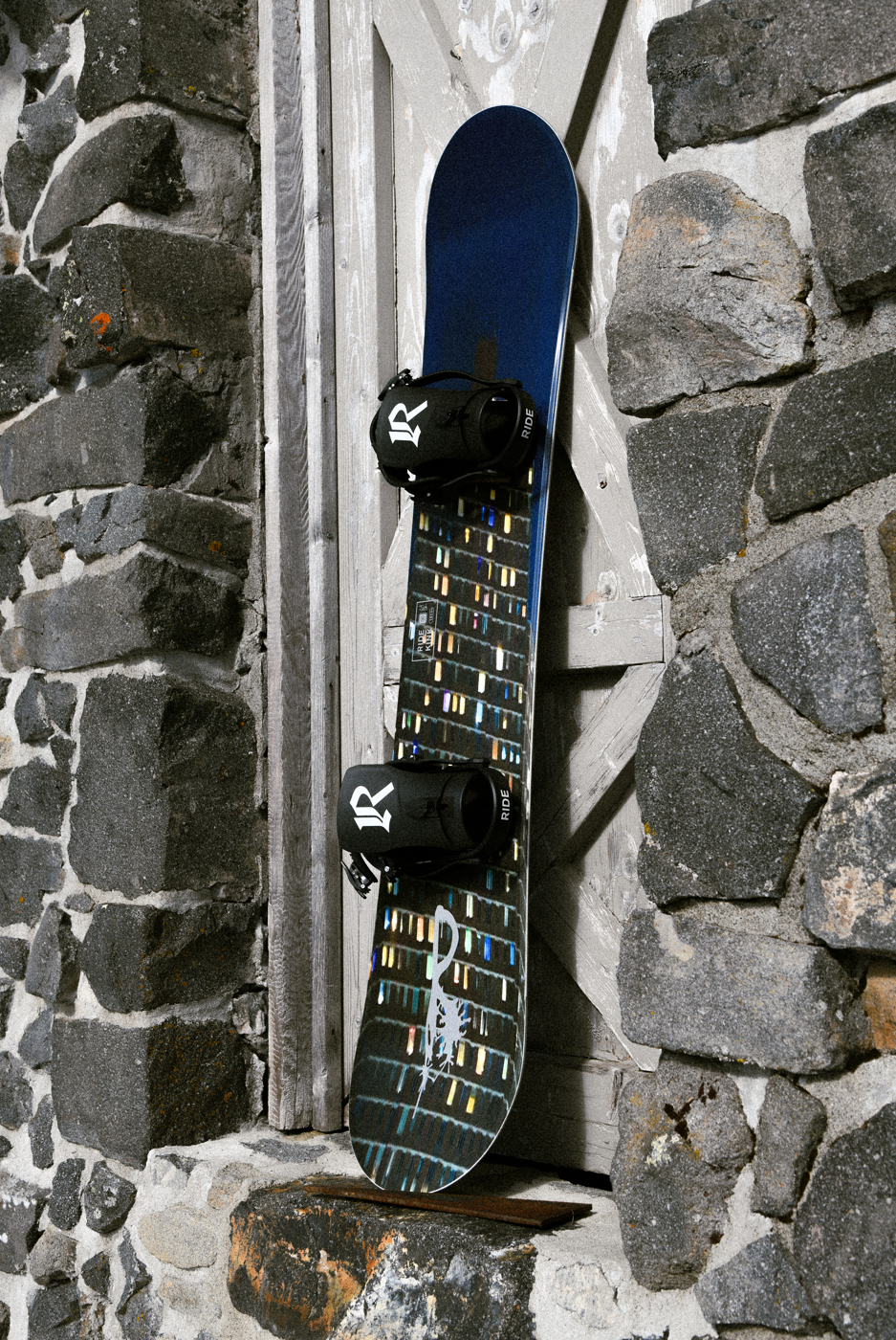 Ride Kink Snowboard 2027 in a lifestyle setting, showing the snowboard's design and graphics on a snow-covered background.
