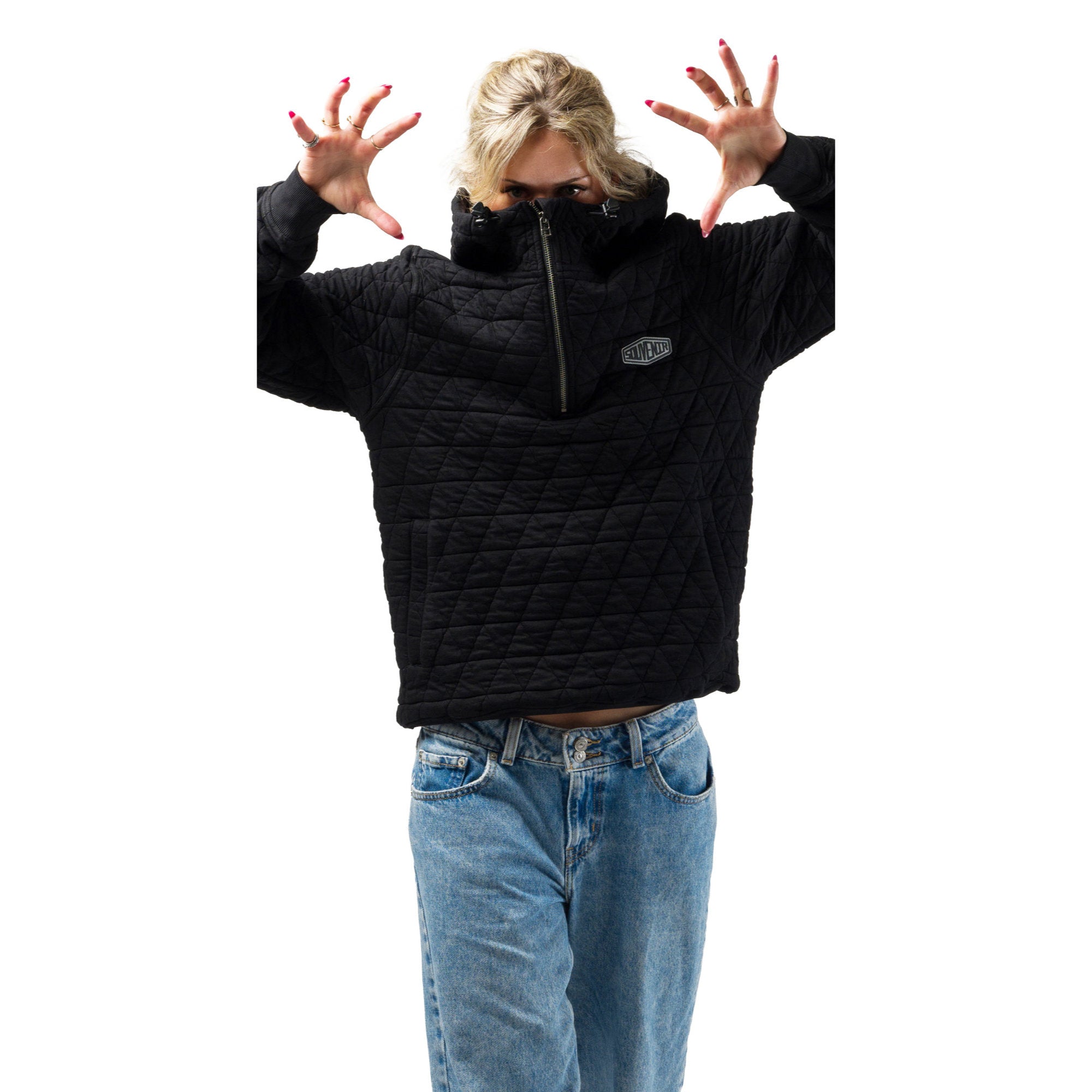 A model wearing a souvenir black quilted half-zip jacket with a small silver logo patch on the chest, paired with blue jeans, posing with hands raised against a solid white background.